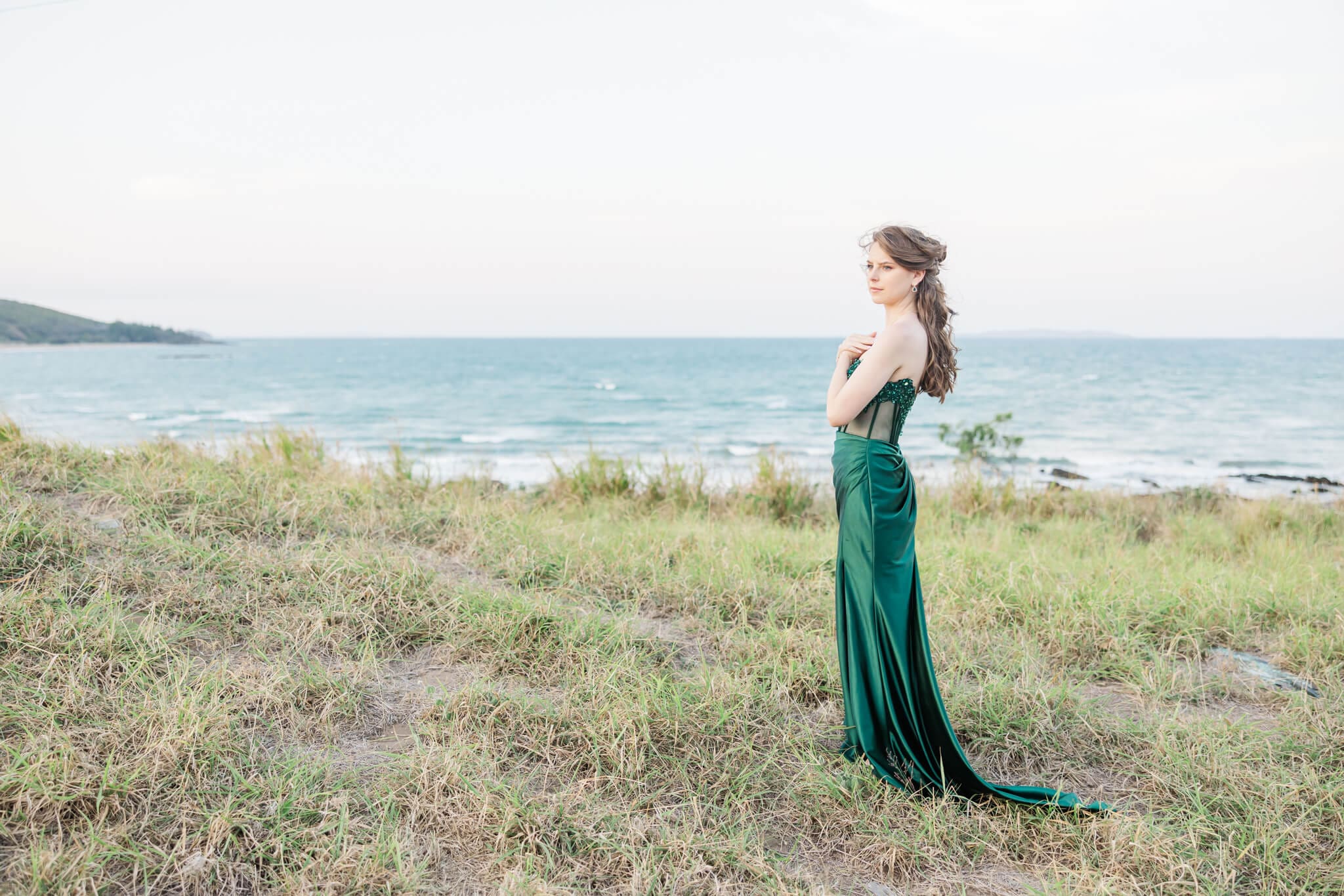 High School senor in an emerald green dress from Oak and Valentine, standing on a hill near the ocean. Photographed by Julie-Anne Photography.