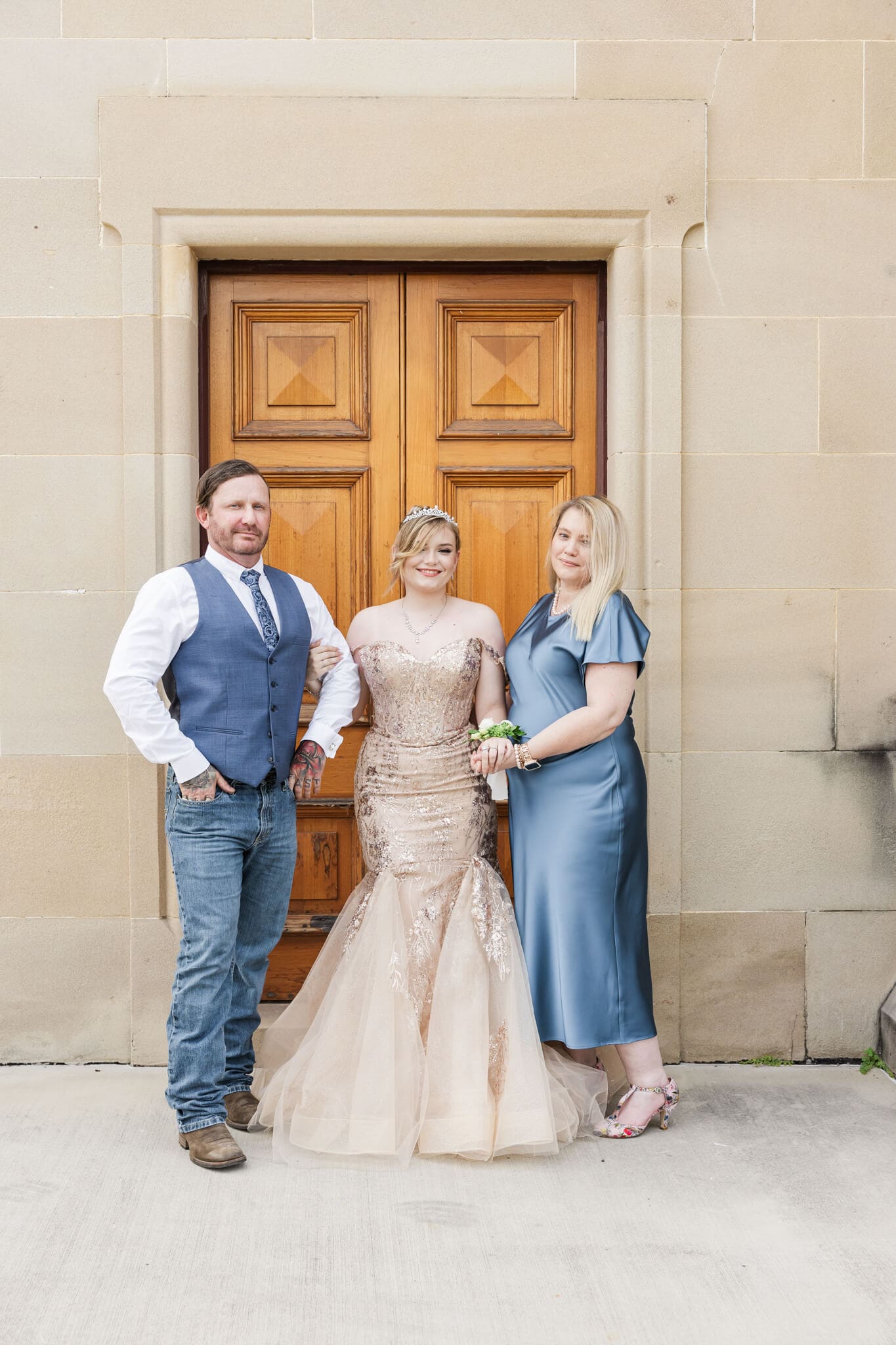 Sweet photo of girl graduate in her formal dress with her parents proudly standing on either side of her.