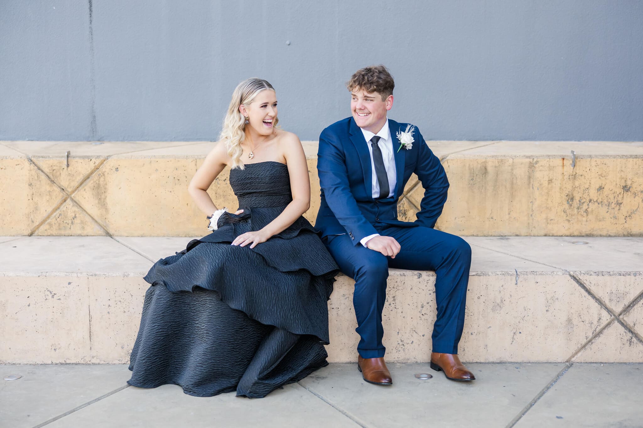 High school seniors having a laugh with each on a stone ledge in their formal dress Rockhampton.