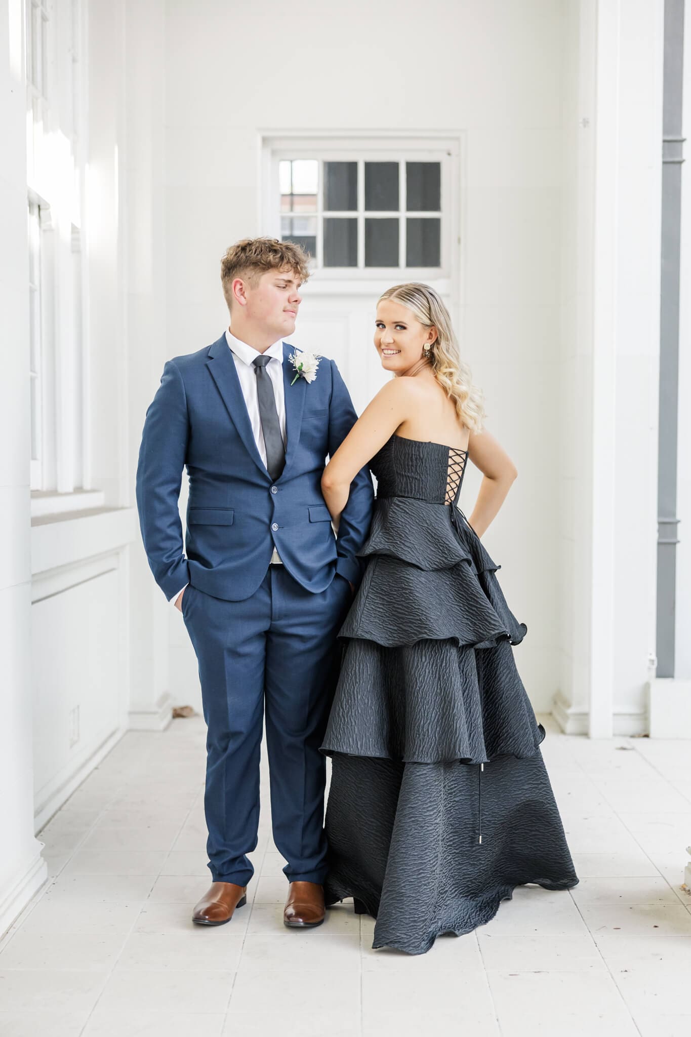 Girl graduate in a black formal dress Rockhampton, holding the arm of her partner who is in a blue suit.
