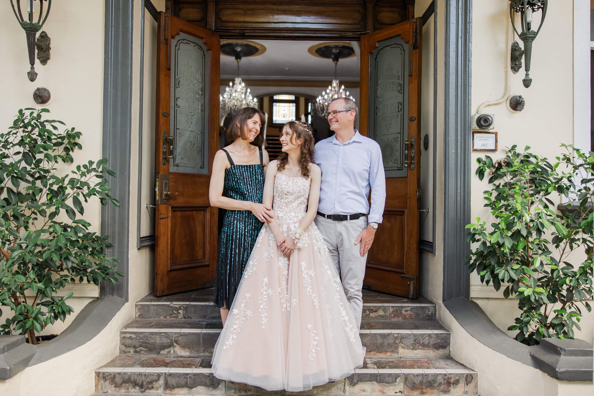 Family photo on formal day, with girl graduate in between her two parents on the steps of The Criterion Hotel, Rockampton, Queensland.
