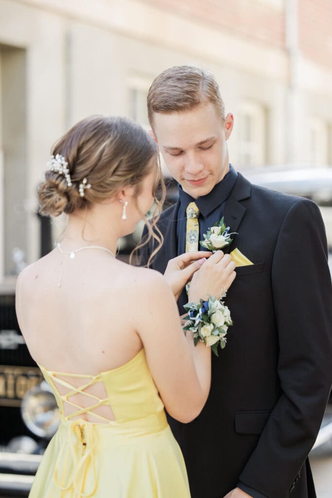 Stunning portrait of girl dressed in formal dress, attaching corsage onto her formal partner's coat jacket.