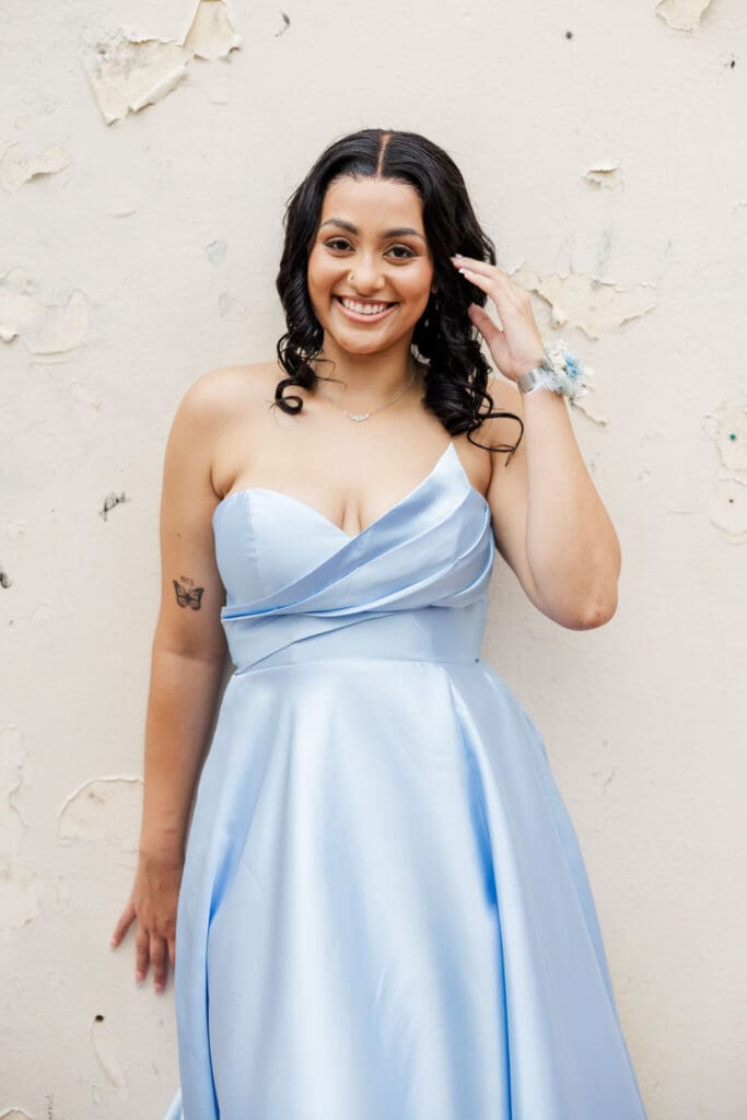 A formal portrait taken near Quay Lane, Rockhampton, Queensland. Graduate girl leans against a cream wall dressed in a sky blue formal dress.