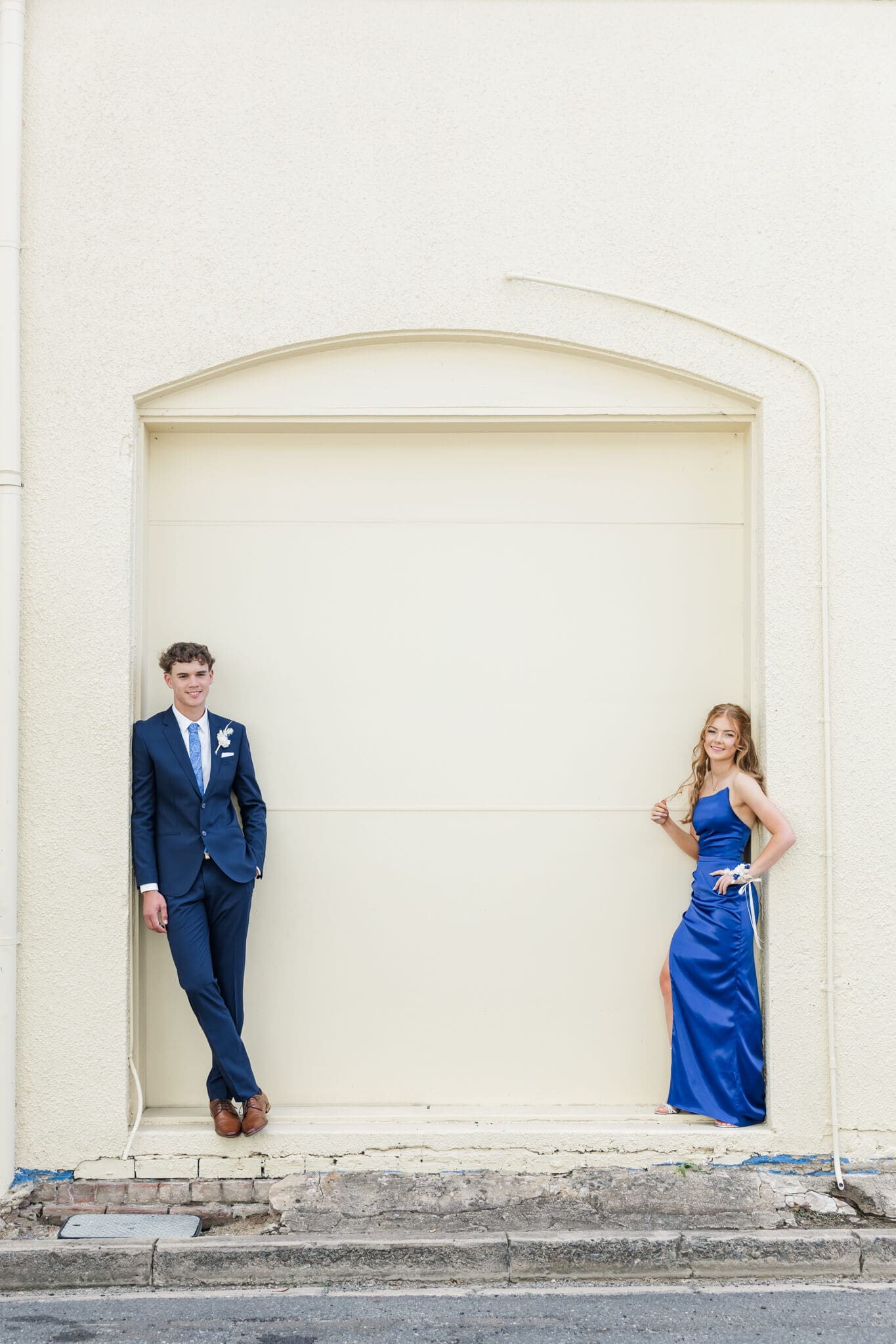 Two high school seniors pose for their formal photos in front of a cream wall in Quay Lane, Rockhampton, Queensland. Captured by Julie-Anne Photography.