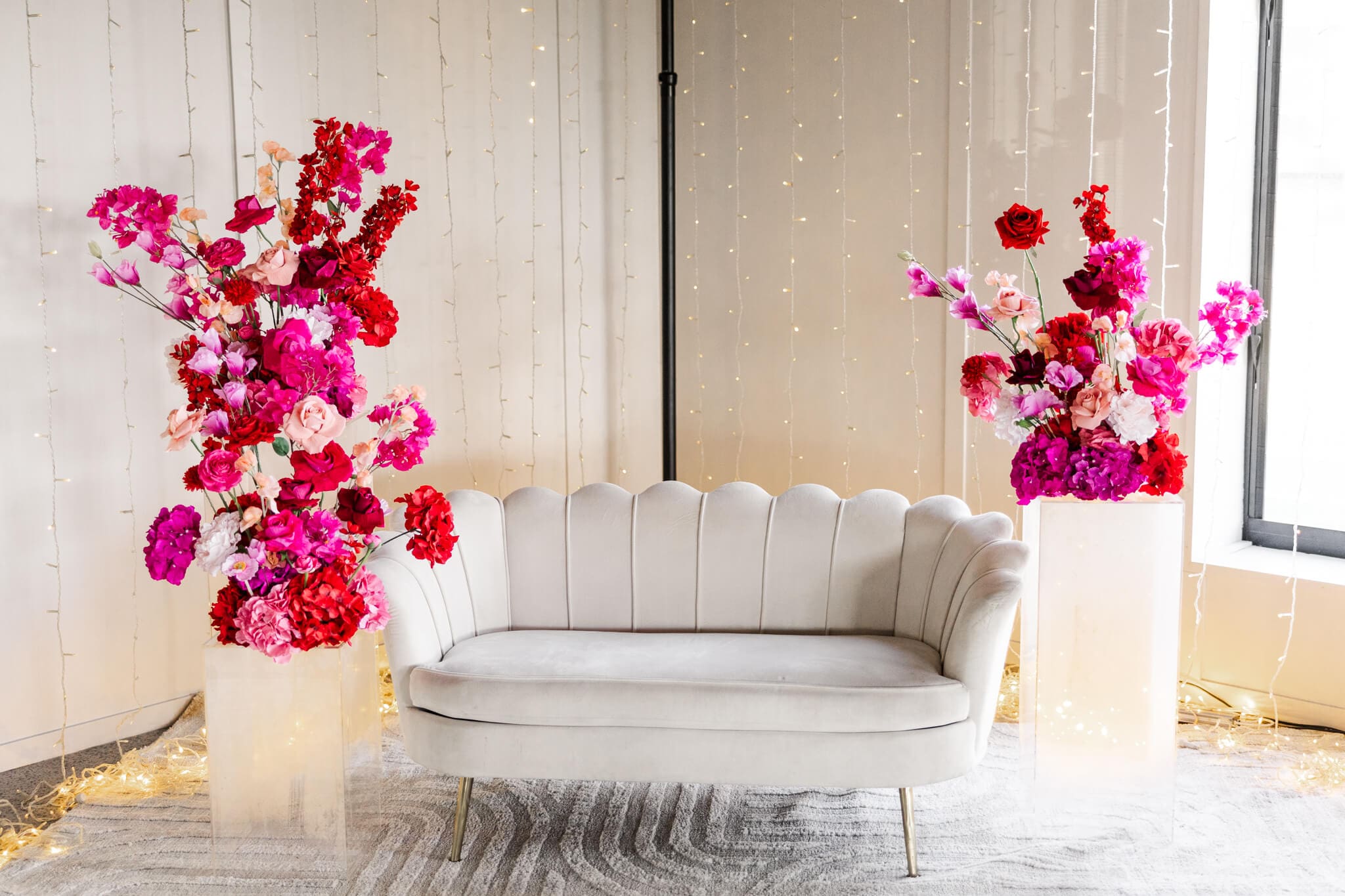 Cream scolloped sofa surrounded by pink and magenta florals, as a set up for a wedding reception.