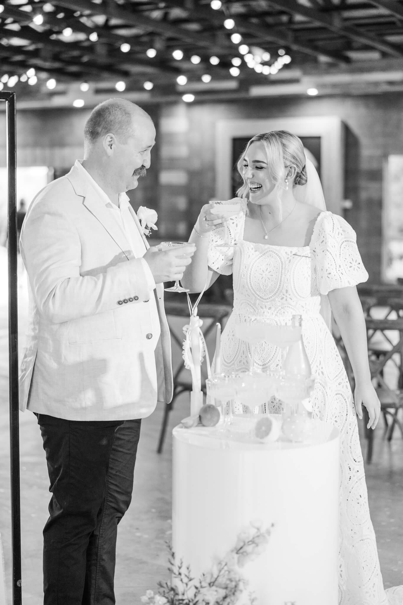 Black and white image of a bride and groom sharing a moment over a champagne tower. Taken at the wedding venue, The Salty Lime Co., by Julie-Anne Photography