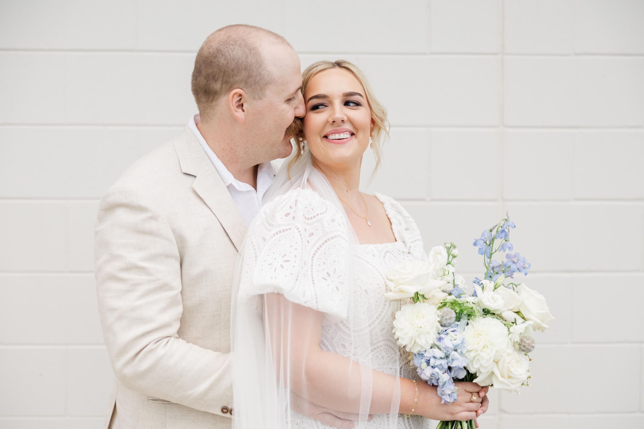Bride and groom sharing a moment against a white brick wall.