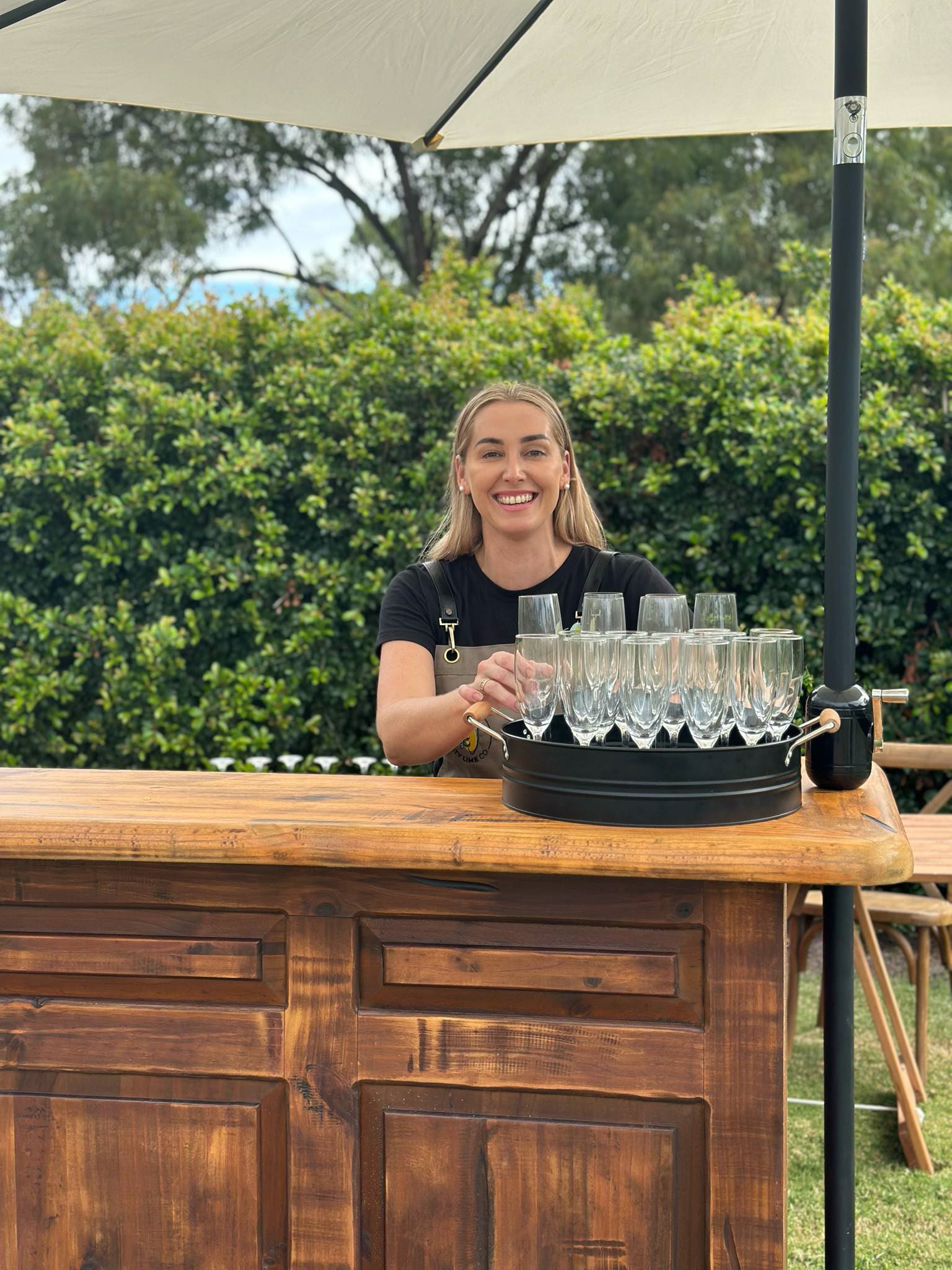 Lady serving drinks behind a wooden bar outside.