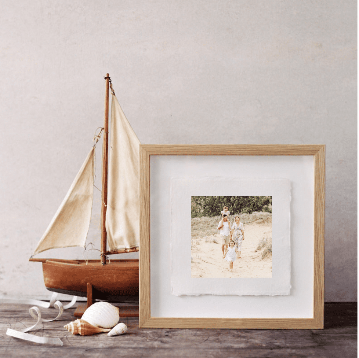Wooden photo frame set next to a small replica boat on a wooden bench. Contains photo of a family where Dad and Mum are walking holding hands in the background while the two children are running ahead in the foreground.