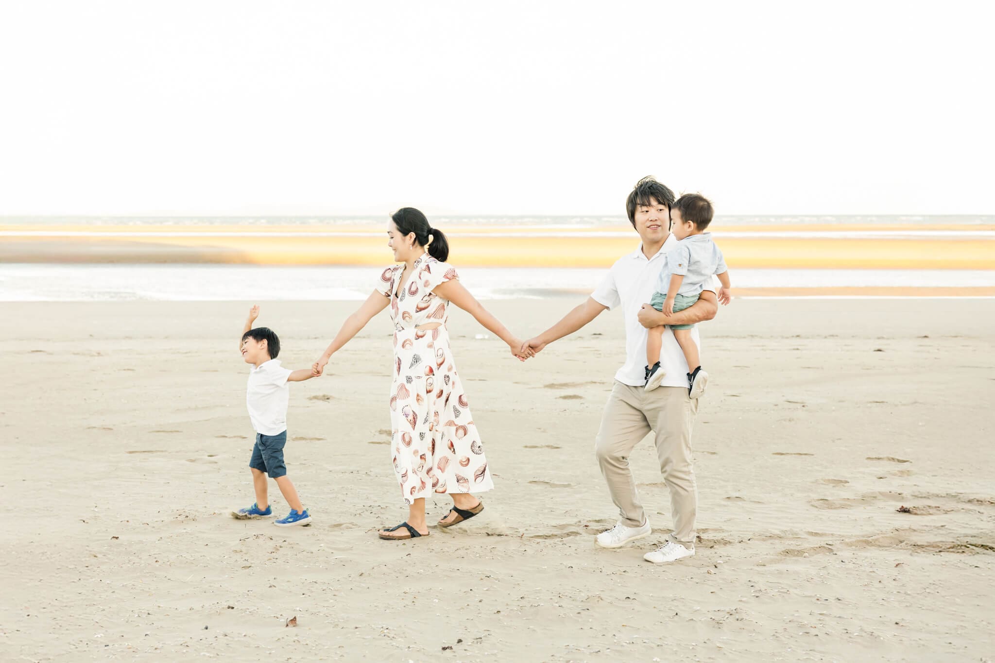 A family photo captured by Julie-Anne Photography of a family of four including Dad, Mum and two little boys, walking along a beach.