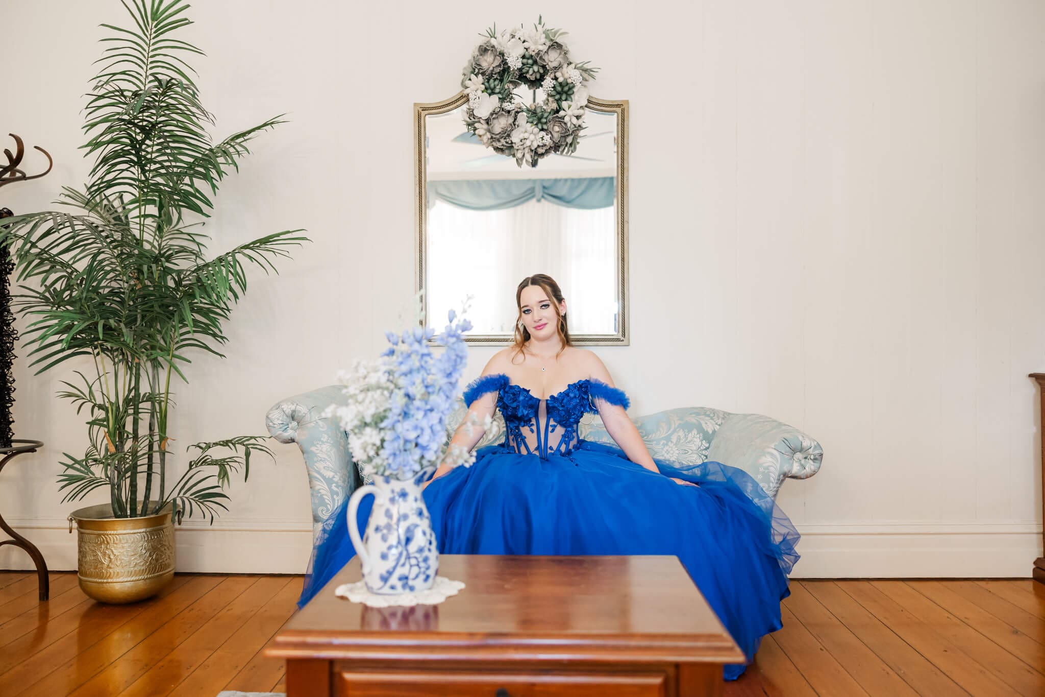 Graduate wearing a formal dress from Rockhampton, royal blue, seated on an old fashioned couch.