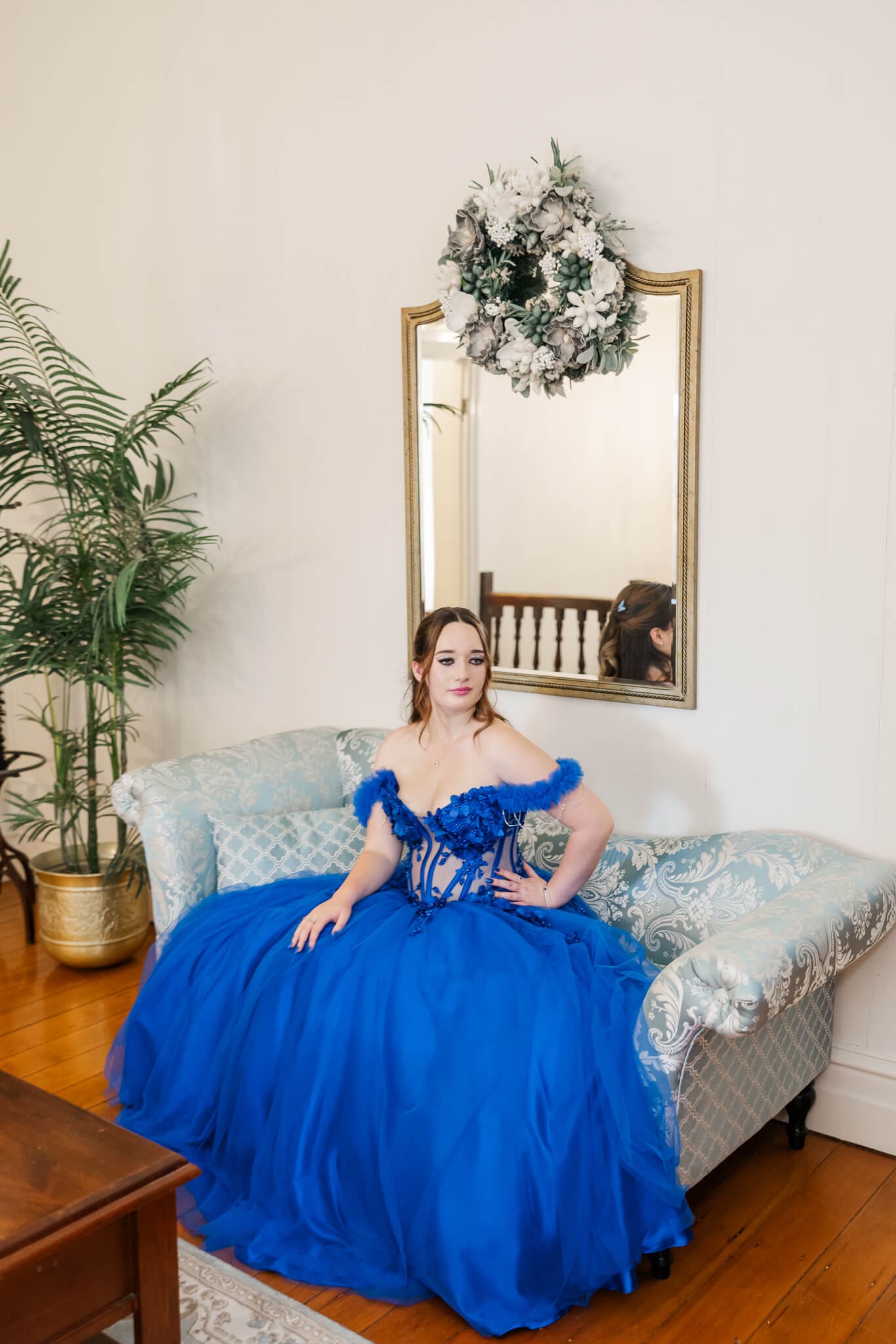 Graduate wearing a formal dress from Rockhampton, royal blue, seated on an old fashioned couch.