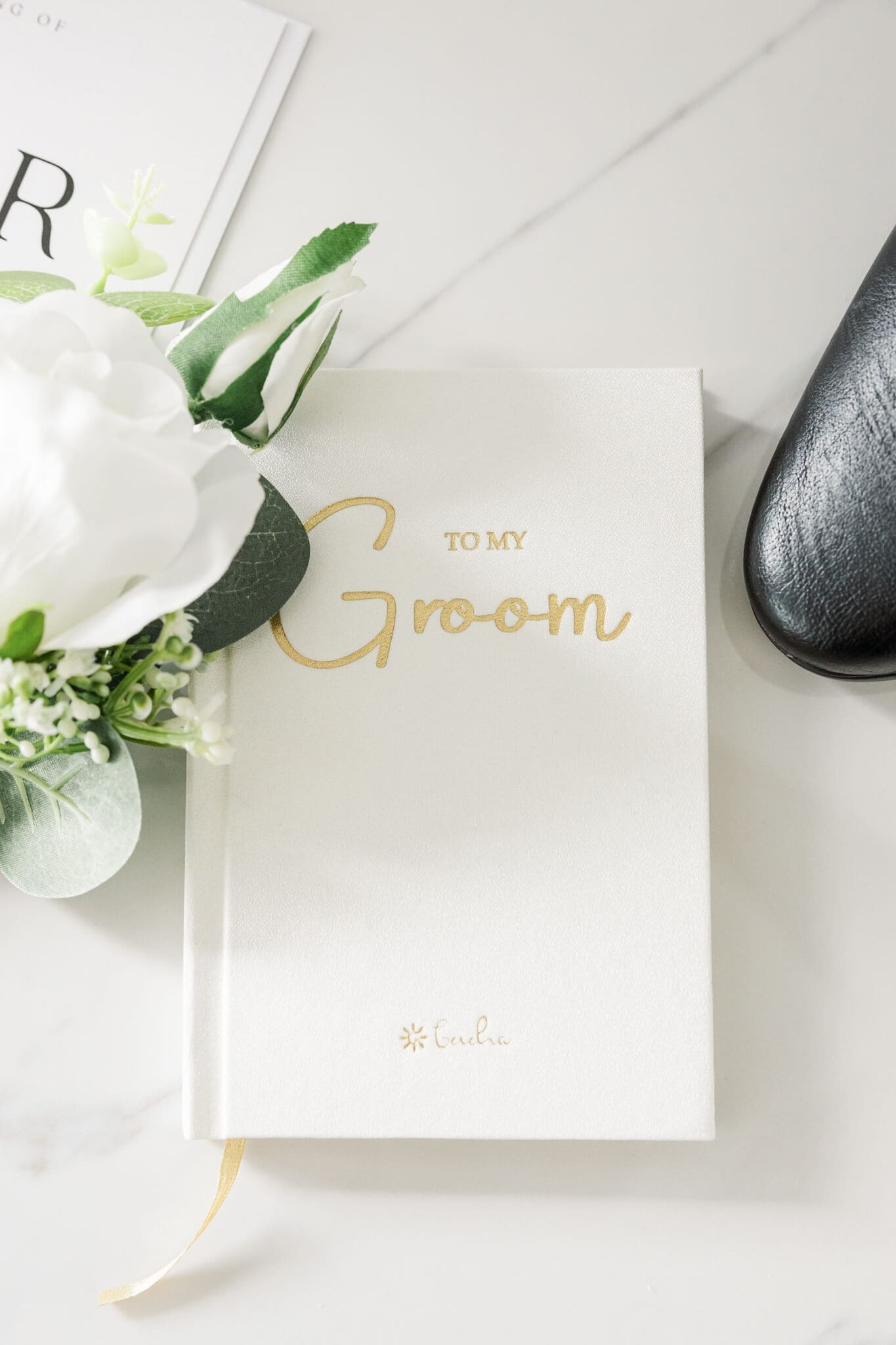 Groom details including white book with gold writing from bride, shoes and corsage.