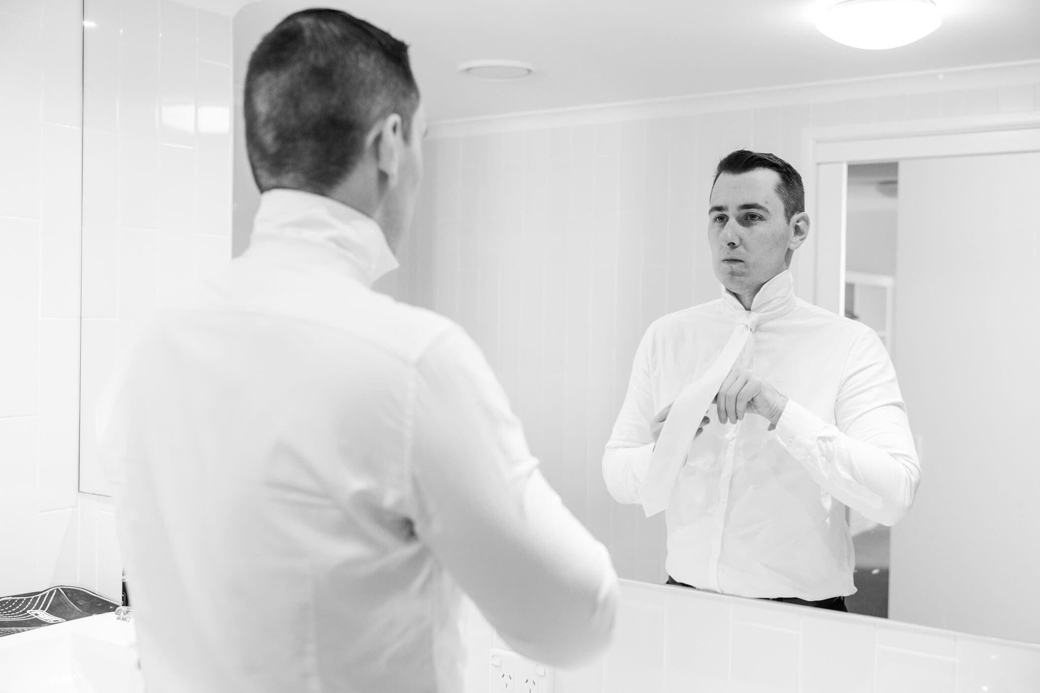 Groom tying his tie in preparation for his wedding. Captured by Rockhampton Wedding Photographer Julie-Anne Photography