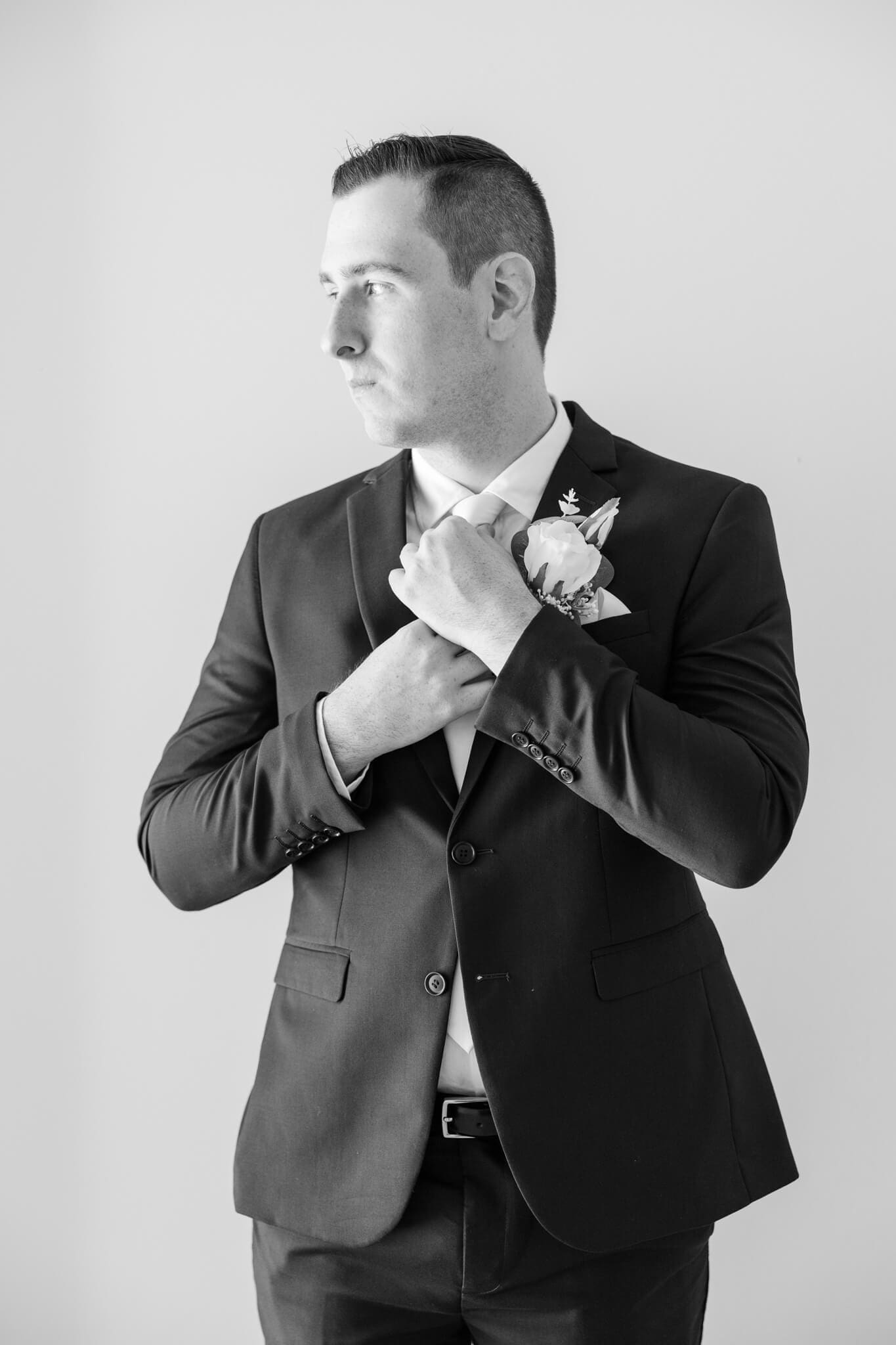 Portrait of groom adjusting his tie while he looks thoughtfully out a window. Captured by Julie-Anne Photography, Rockhampton, Queensland.