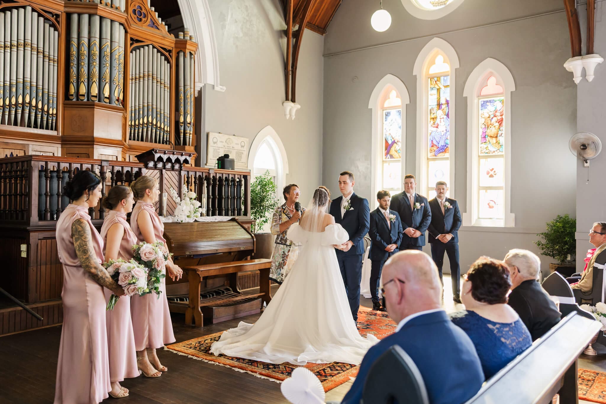 Beautiful ceremony settings at the Church Events Venue in Rockhampton. Stained glass windows letting in natural light while the bride and groom exchange wedding vows.