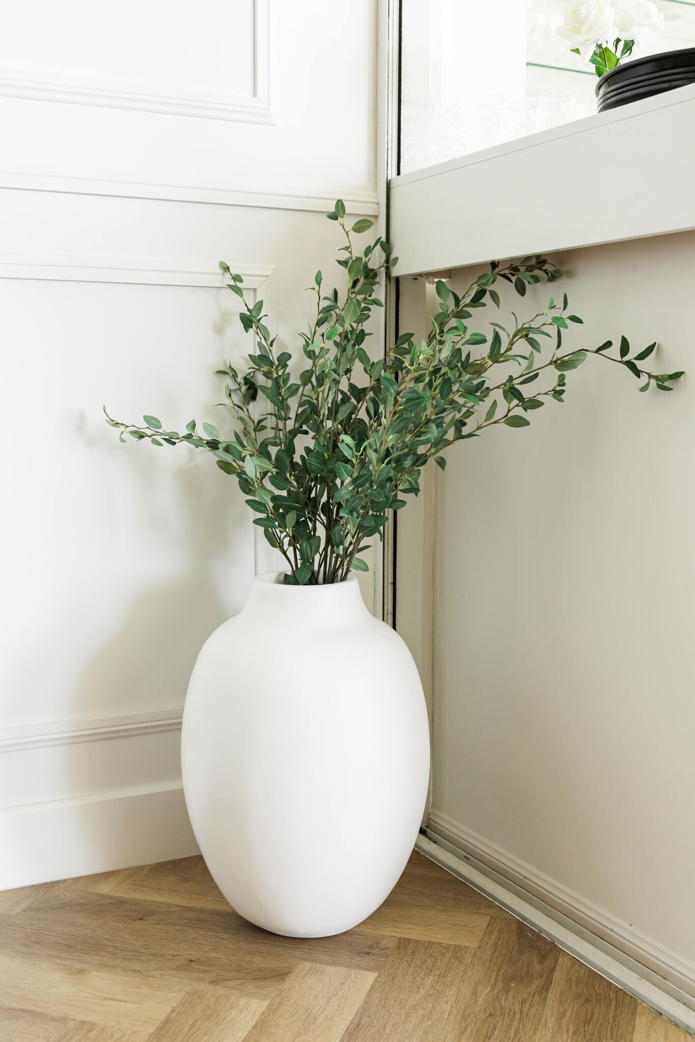 An indoor white pot with a green plant flowing out of it.