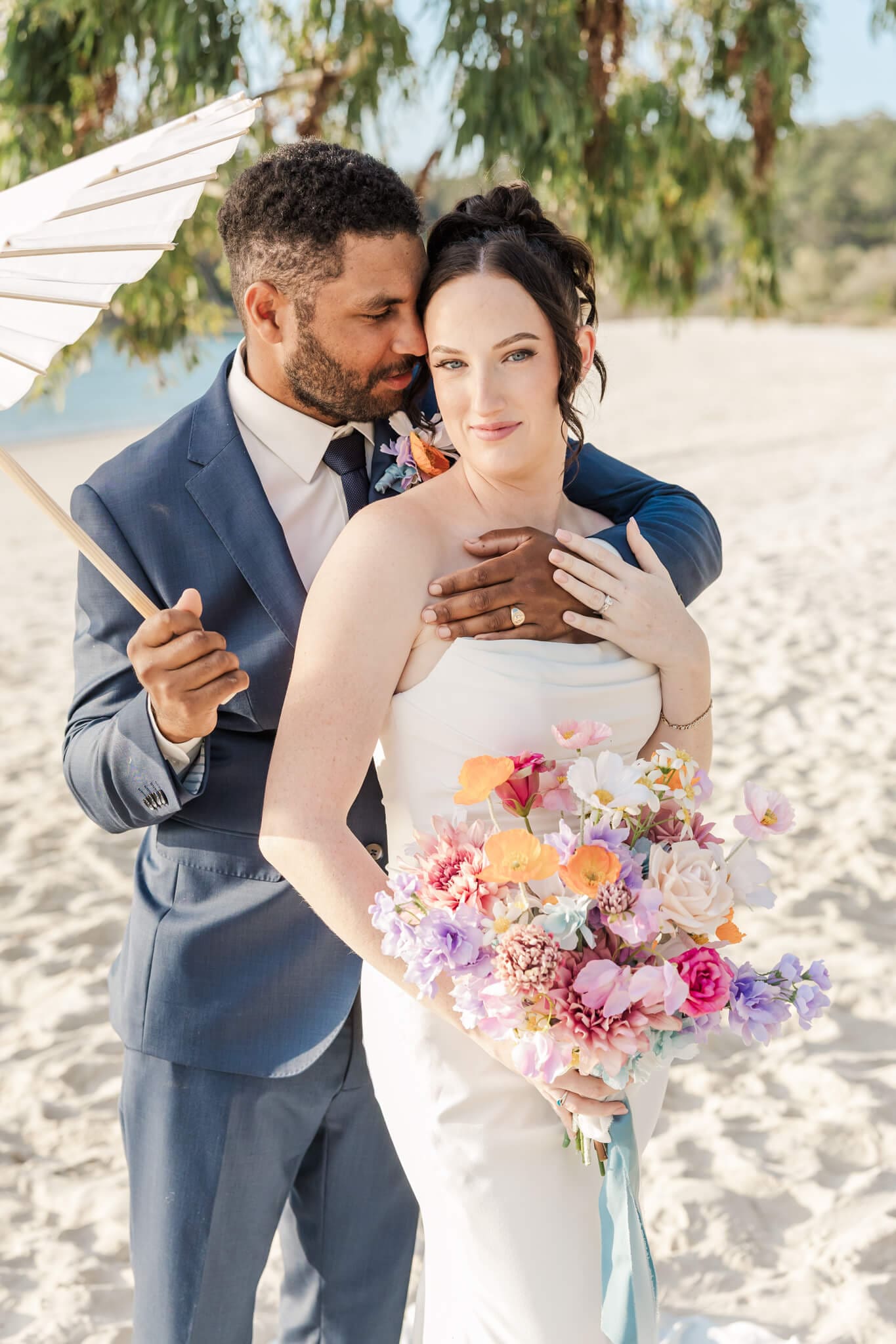 Stunning bride and groom portrait on a beach located at Great Keppel Island Hideaway. Groom holds umbrella while he embraces his bride.