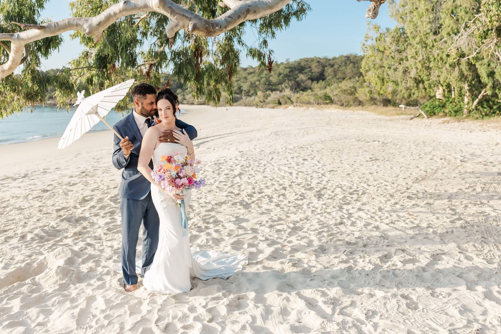 Stunning bride and groom portrait on a beach located at Great Keppel Island Hideaway. Groom holds umbrella while he embraces his bride. Captured by Julie-Anne Photography.
