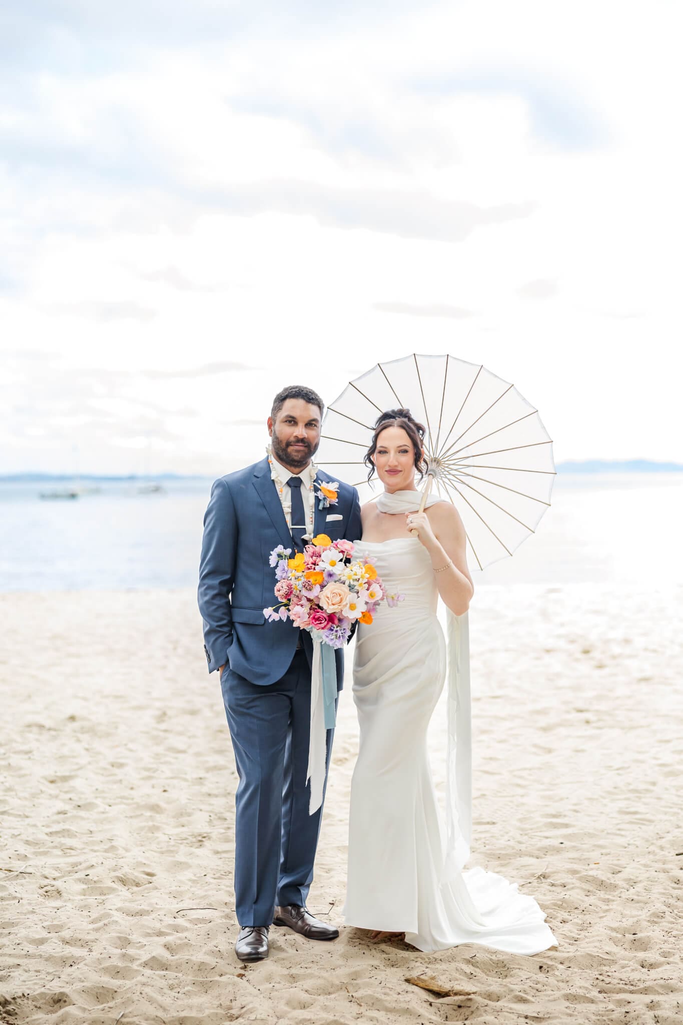 Bride and Groom pose on a beach on Great Keppel Island. Bride holds a parasol and the couple have the ocean behind them in the background.