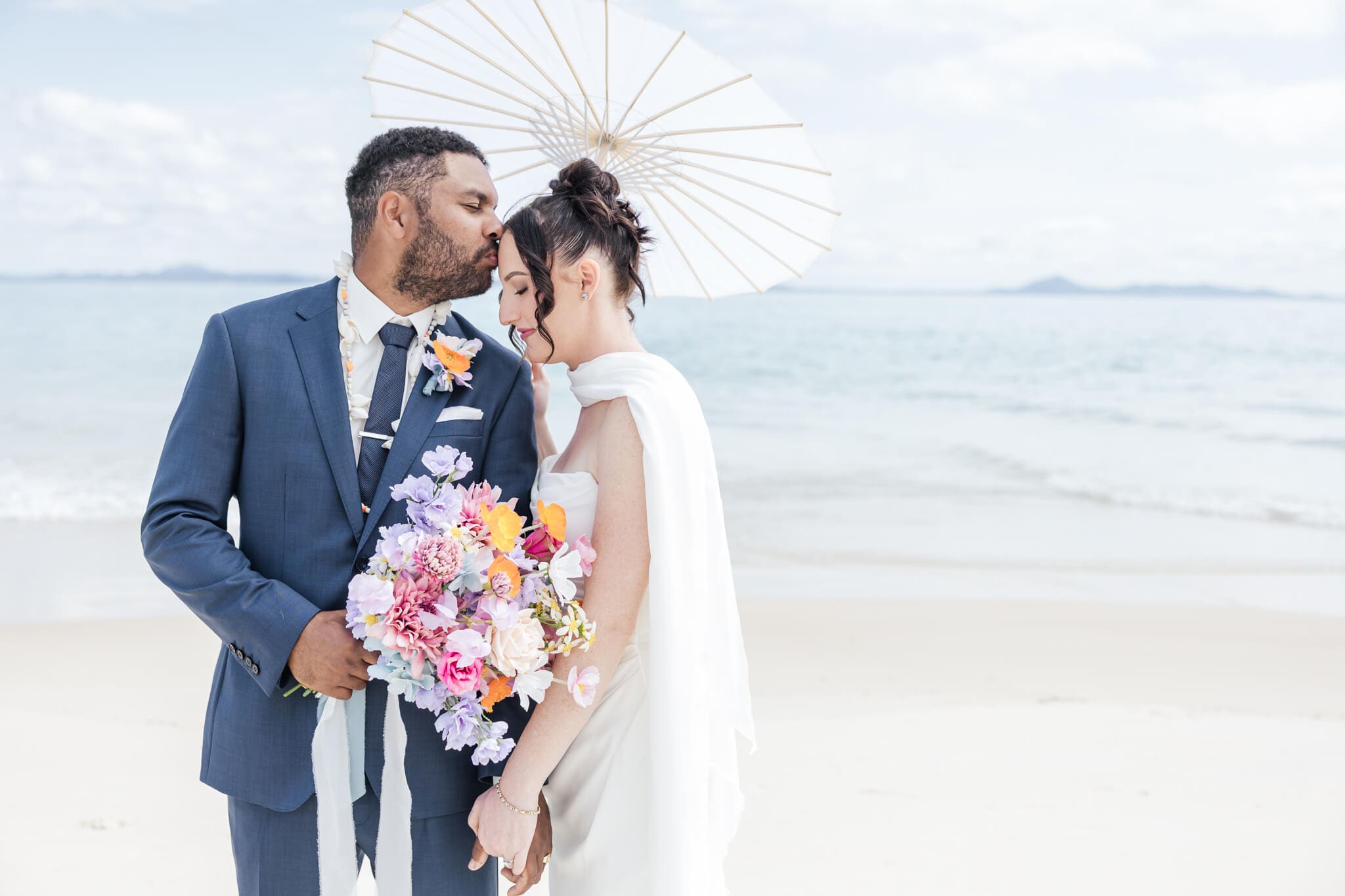 Bride and Groom share a moment on their wedding day. Groom kissing the bride on the forehead on a beach at Great Keppel Island Hideaway.