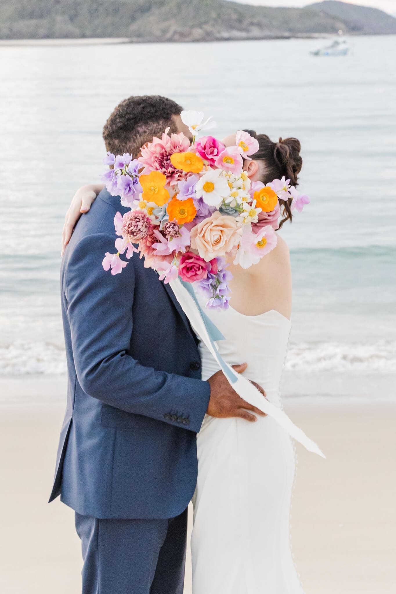 Bride and groom kiss while the bride holds the bouquet up in front of the couple to hide behind.