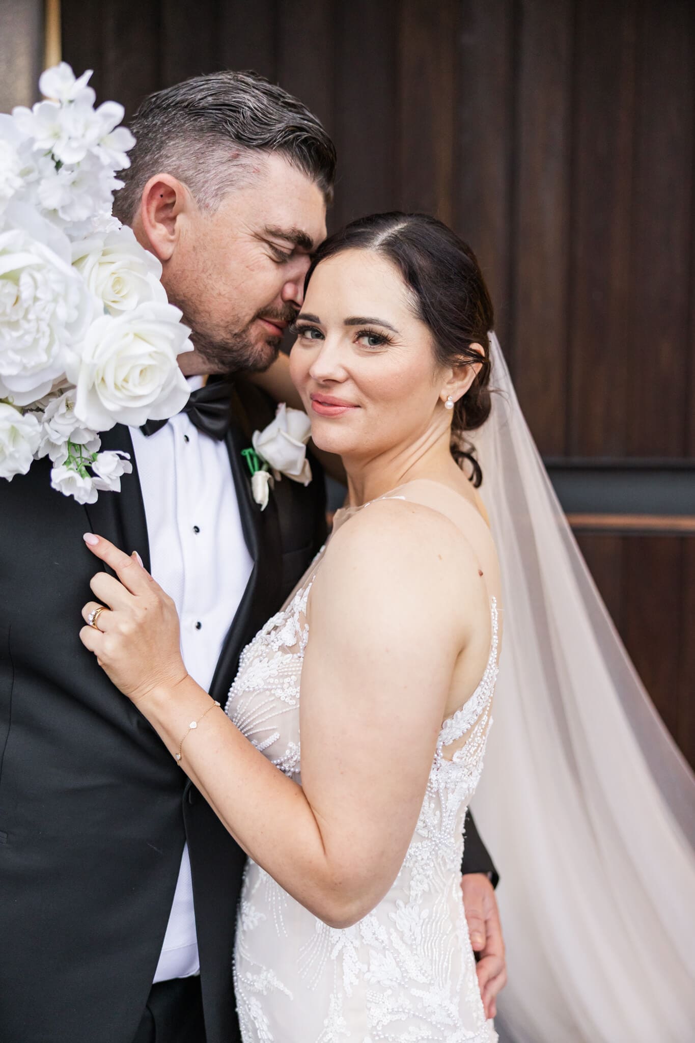 Beautiful wedding image of bride and groom, standing together, brides arm and bouquet around grooms neck while he touches her head with his face. Captured by Julie-Anne Photography, Rockhampton wedding photographer.