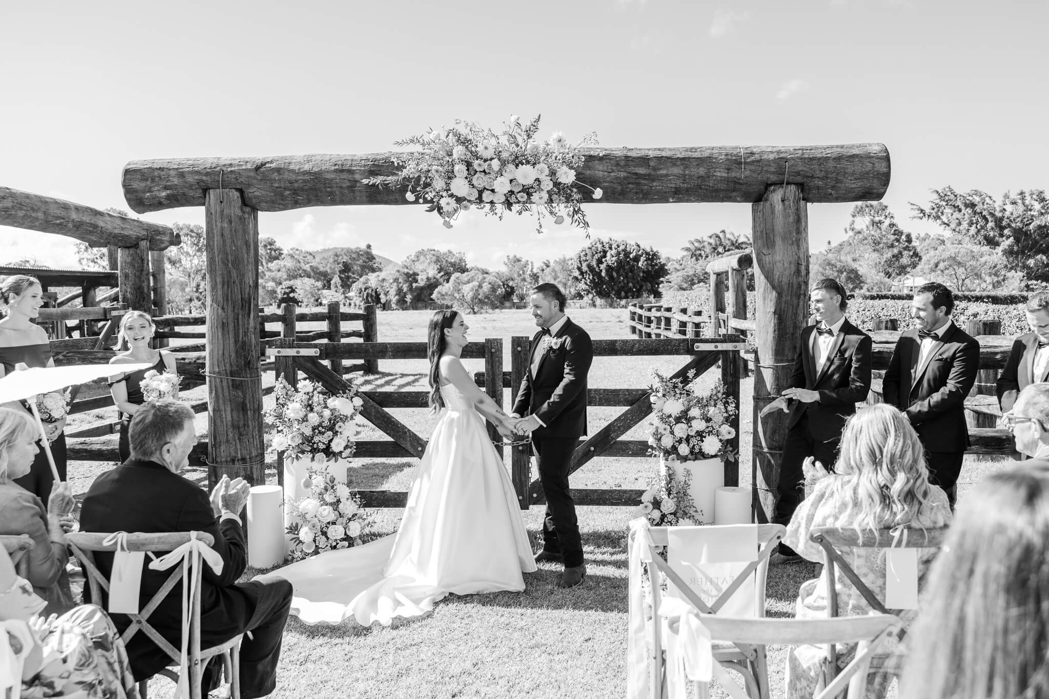 Black and white wedding image captured by Julie-Anne Photography of a bride and groom exchanging vows in front of a set of yard gates. Location Yeppoon, Queensland.