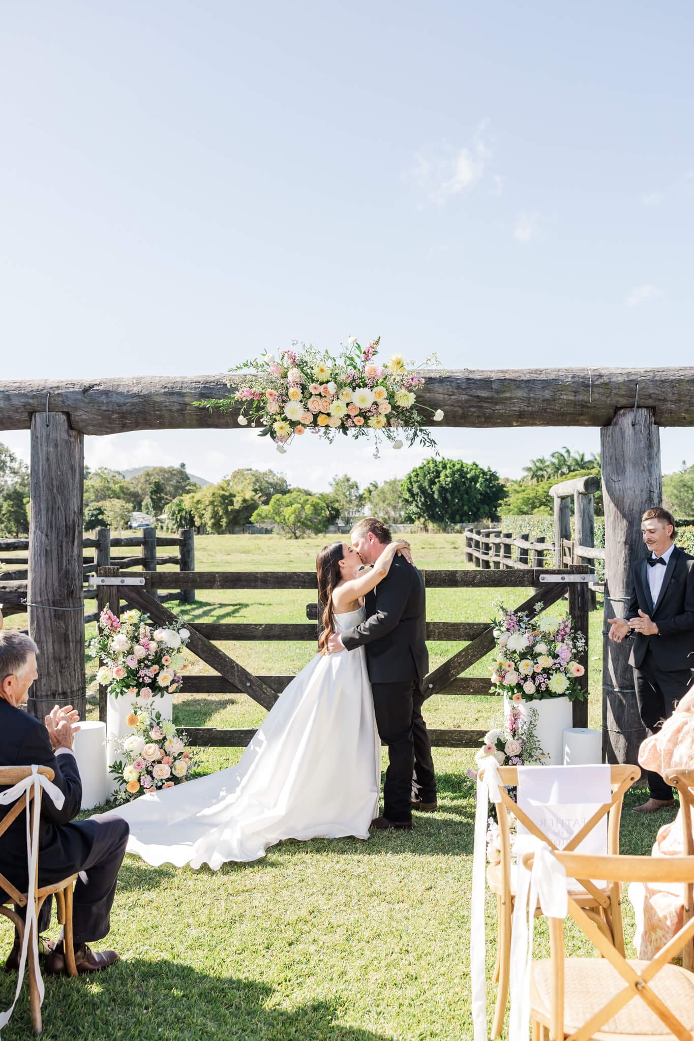 Bride and Groom share a kiss at their wedding ceremony at a Yeppoon wedding venue in front of a wooden gate that is part of a set of yards.