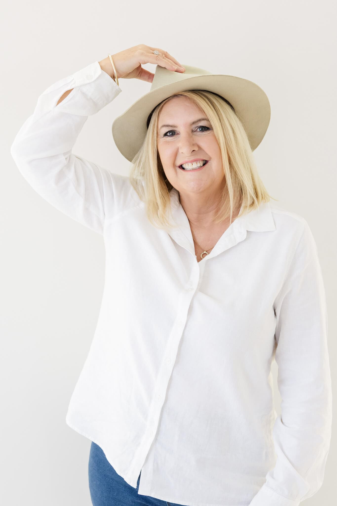 Branding photo of a marriage celebrant dressed in a white blouse and blue jeans, wearing a cream wide brimmed hat.