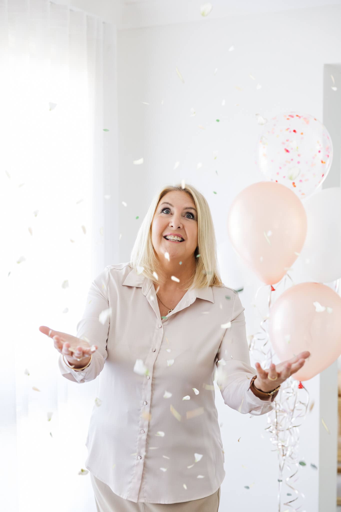 Branding photo of a marriage celebrant, catching confetti and standing near balloons in a white blouse.