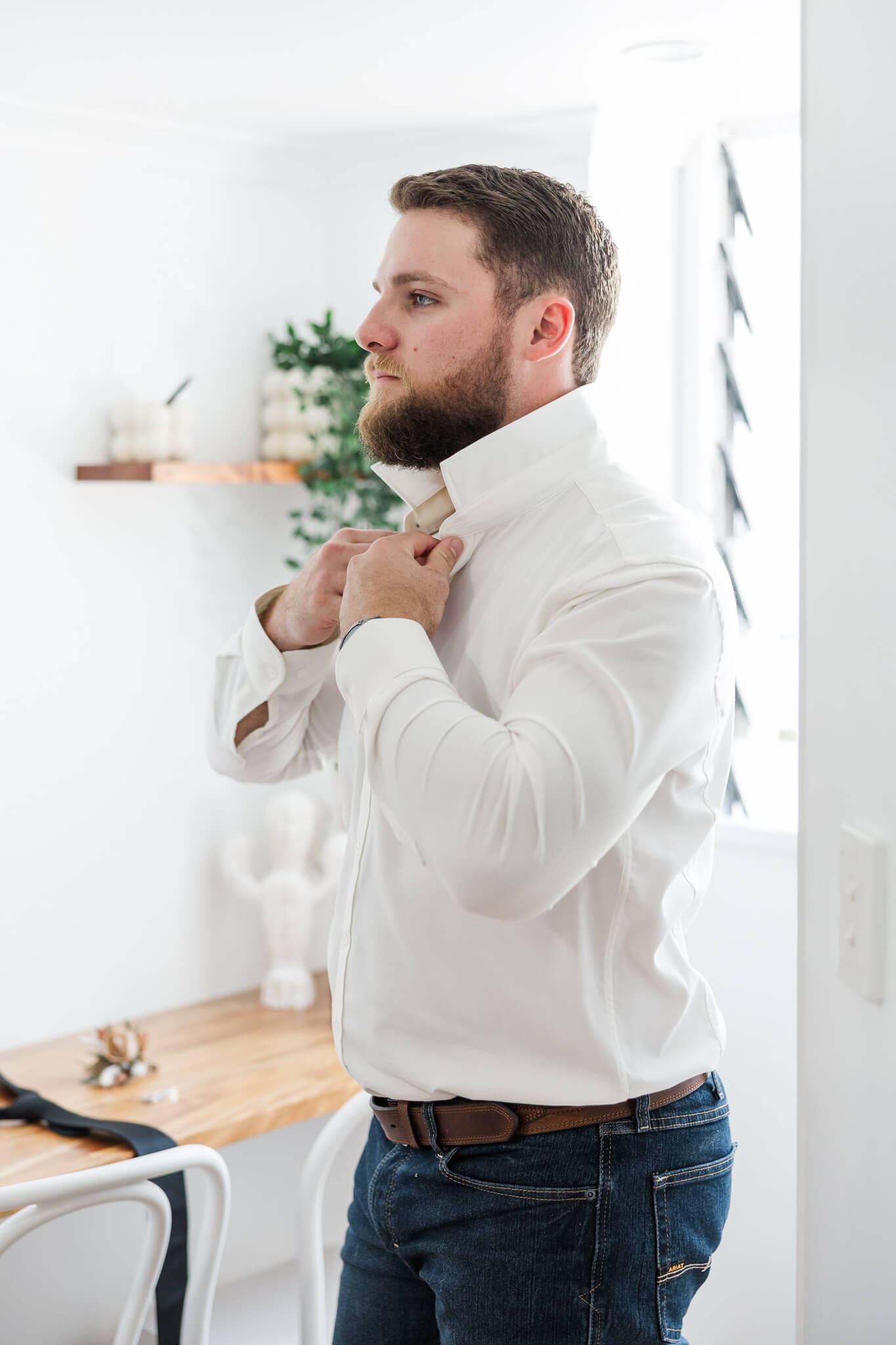 Groom adjusts his collar as he dresses himself ahead of his wedding day. 