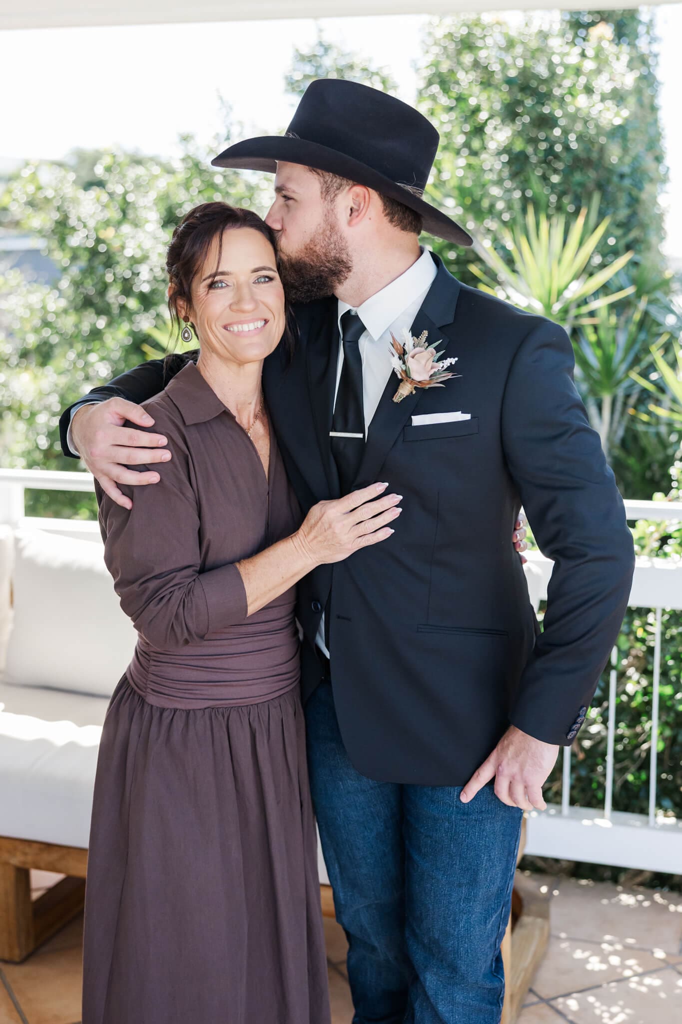 Portrait of a groom and his mum before his wedding ceremony. Groom is reaching over and kissing his mums temple in a loving gesture.