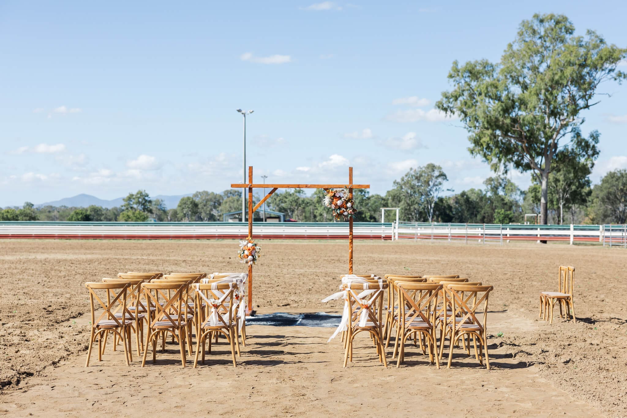 Wedding ceremony set up in the arena at Paradise Lagoons Rockhampton, with a decorated wooden arbour and wooden chairs.