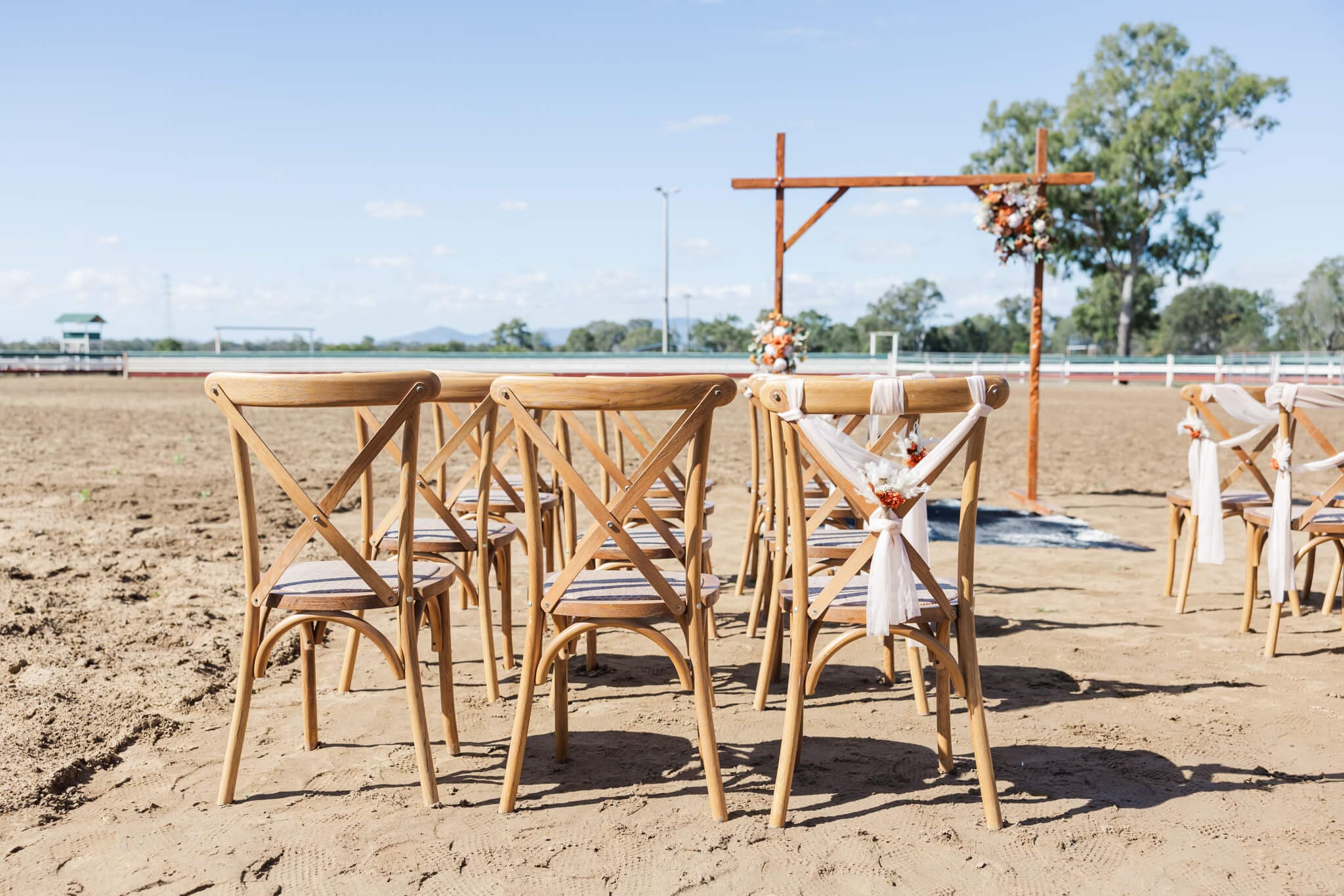 Wedding ceremony set up in the arena at Paradise Lagoons Rockhampton, with a decorated wooden arbour and wooden chairs.