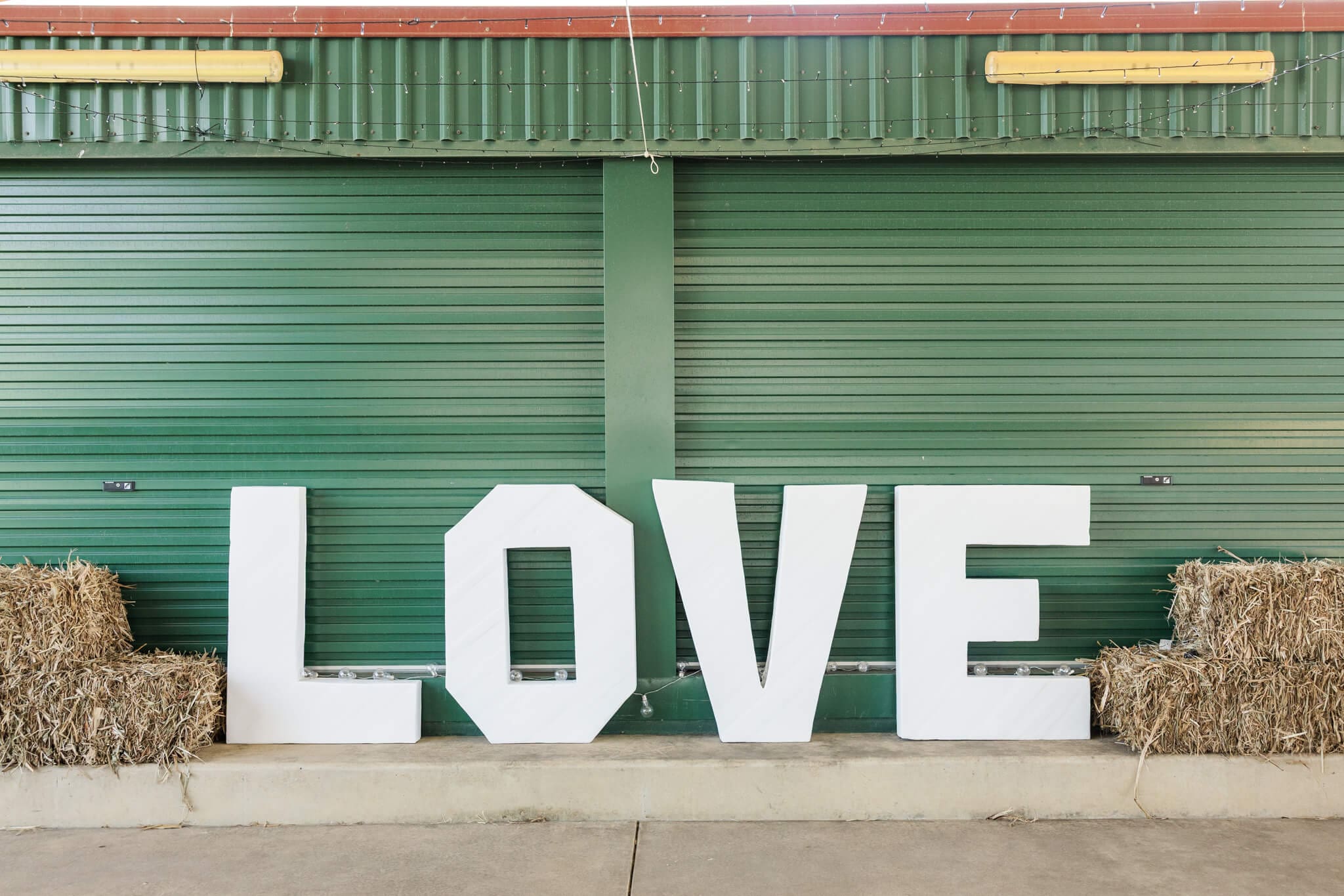 Wedding sign that spells 'love' against a green shed with hay bales next to it.