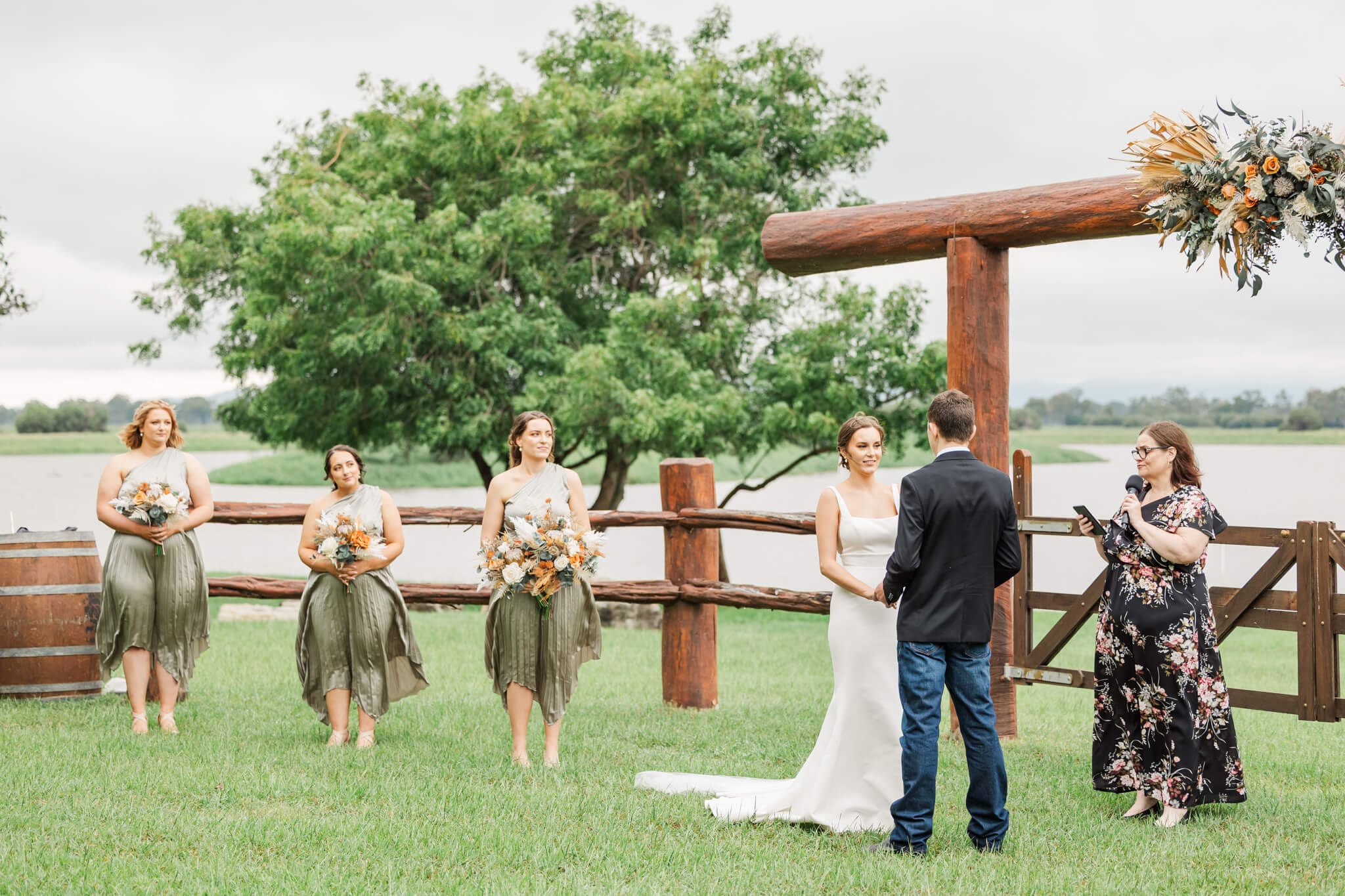 Wedding ceremony at Paradise Lagoons Rockhampton. The bride and groom exchange vows in front of a set of rails and gates next to a lagoon.