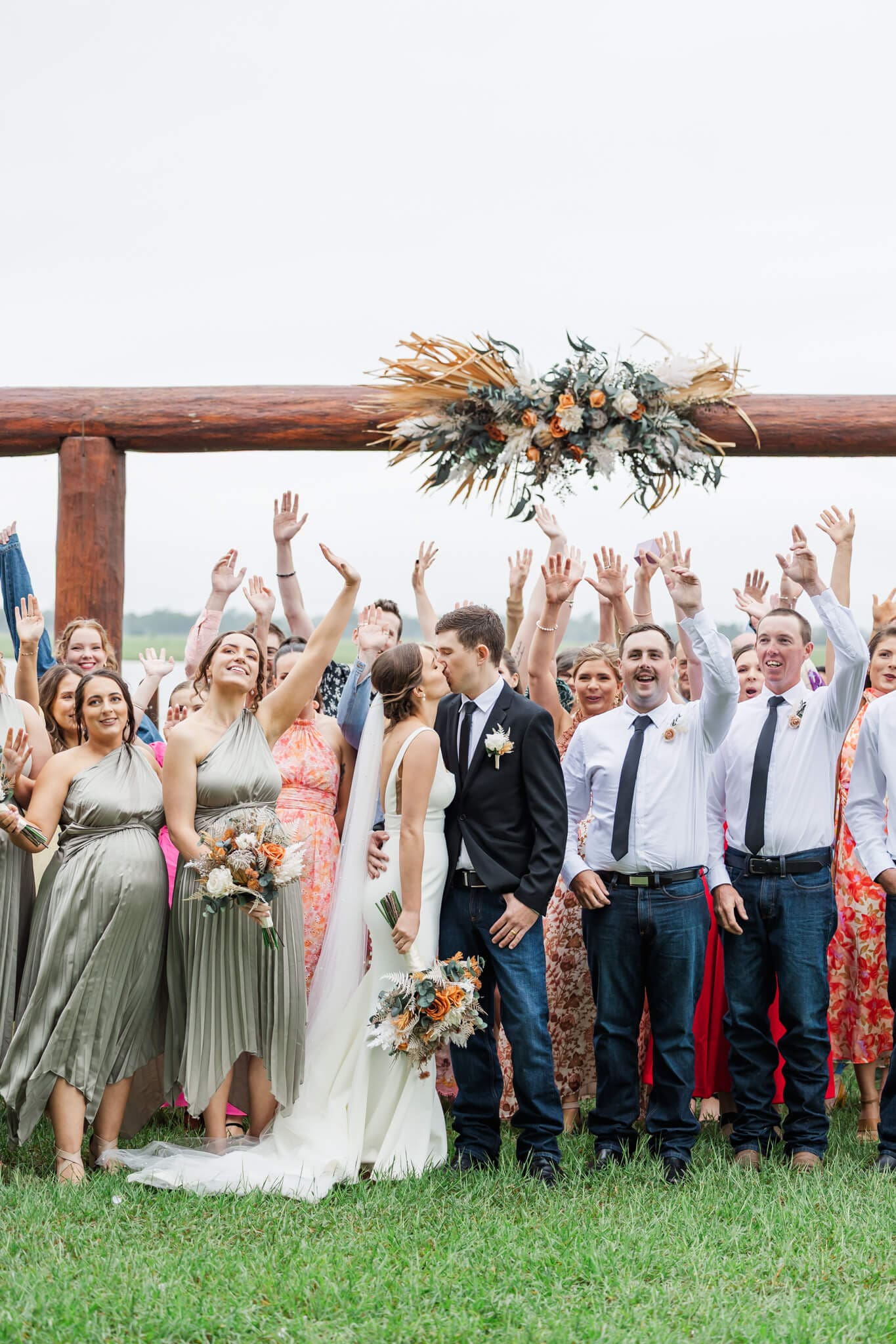A bride and groom exchange a kiss while they are surrounded by family and friends attending their wedding.