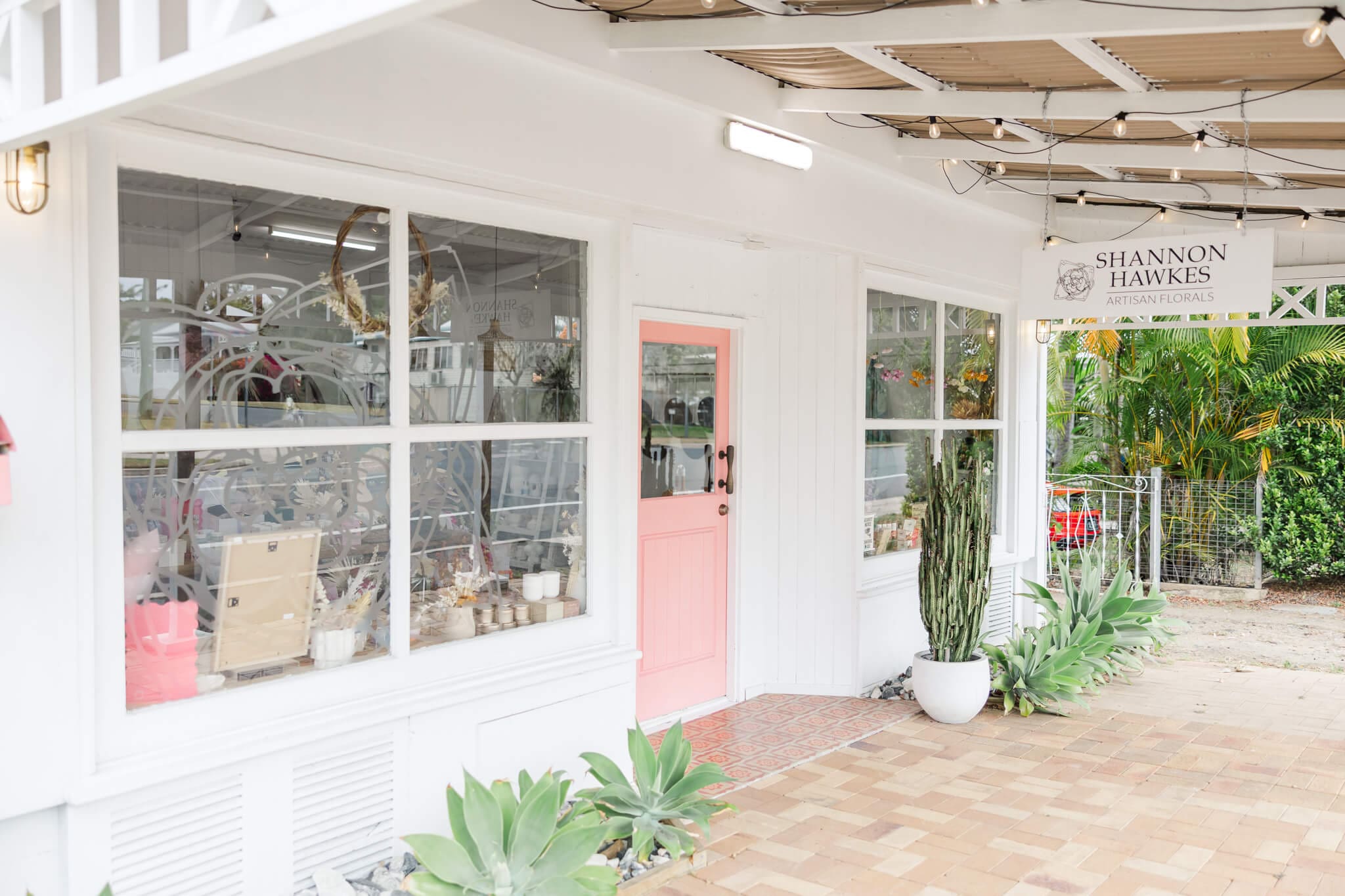 Exterior of Shannon Hawkes Rockhampton shop front. Beautiful pink door, white building and potted plants on a patio.