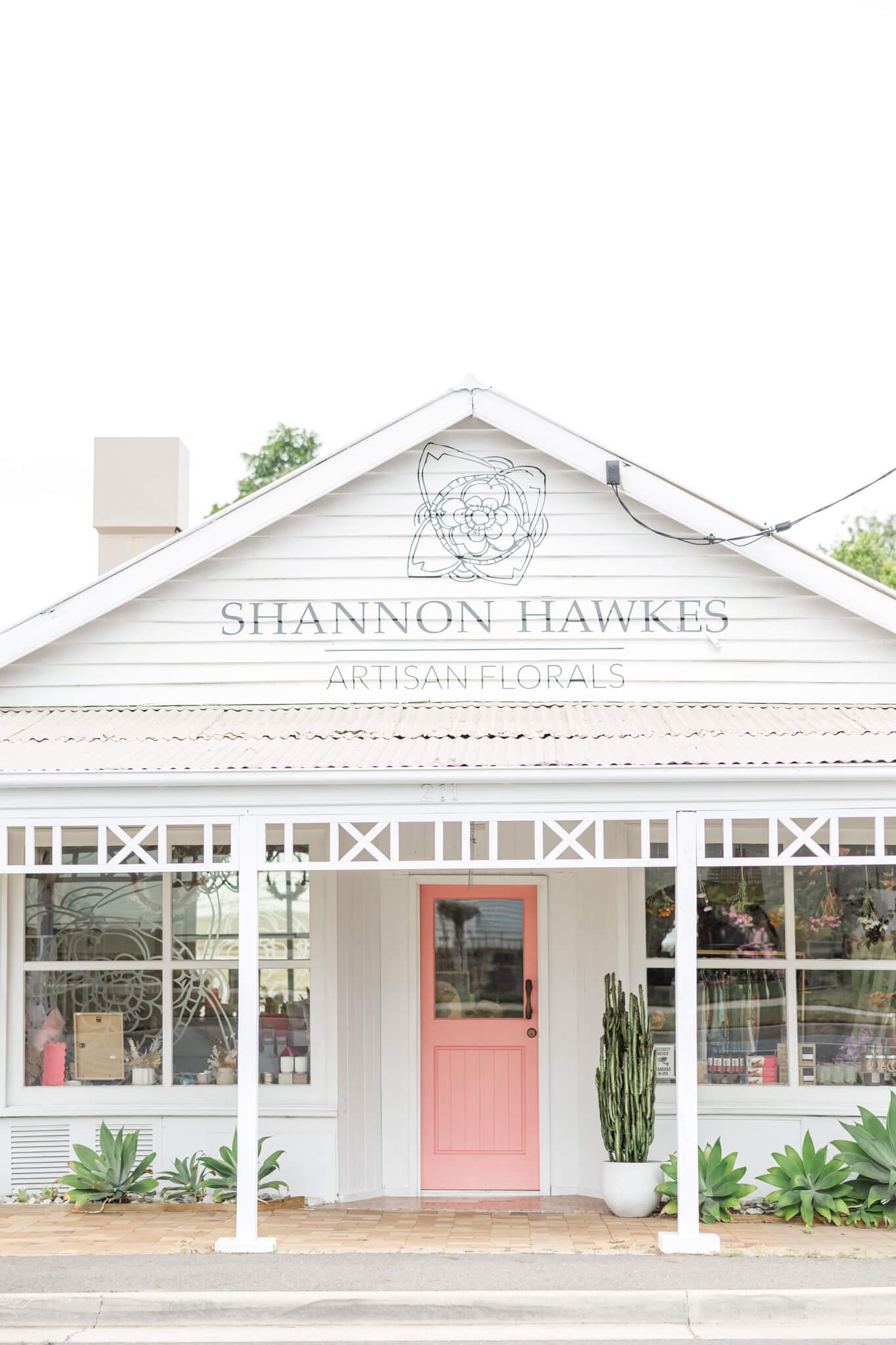 Exterior of Shannon Hawkes Rockhampton shop front. Beautiful pink door, white building and potted plants on a patio.