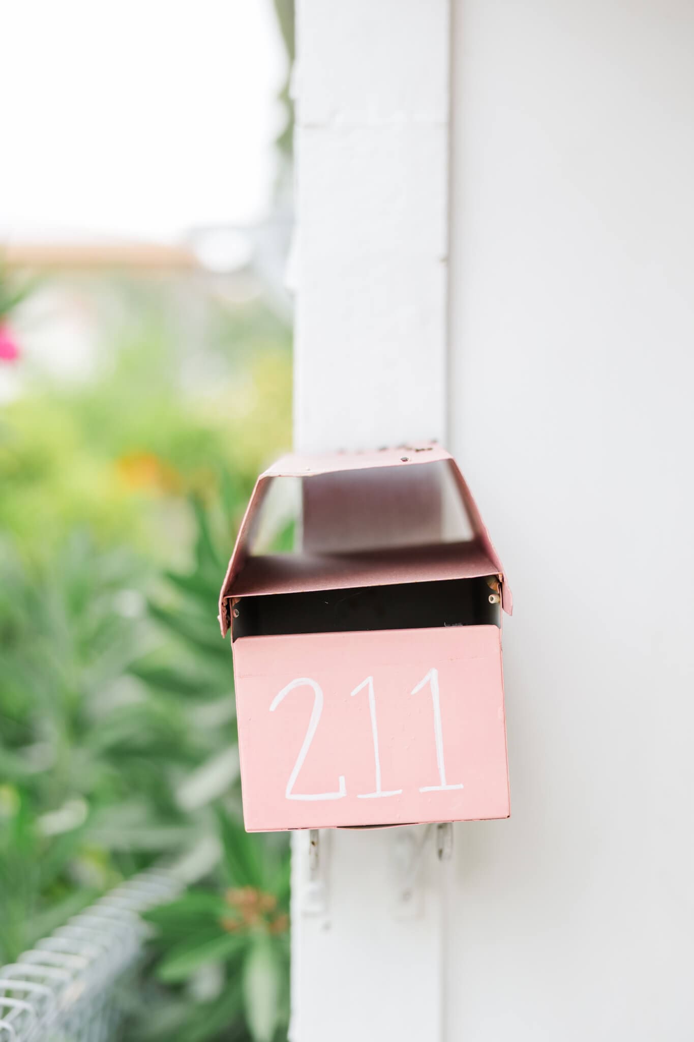A cute pink mailbox on a white wall of a building.