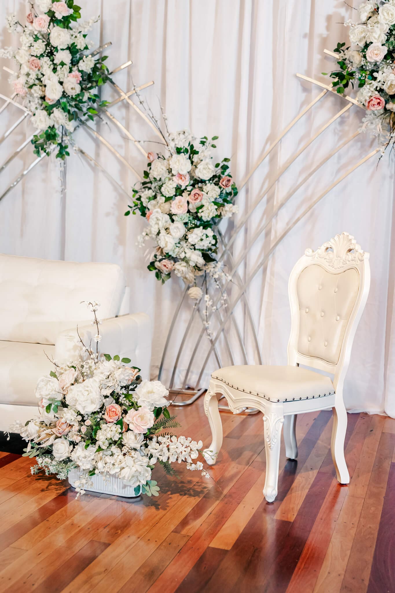 Beautiful styling by a wedding hire Rockhampton business, Stylish Events and Hire. A white chair and sofa surrounded by white, pink and cream florals.