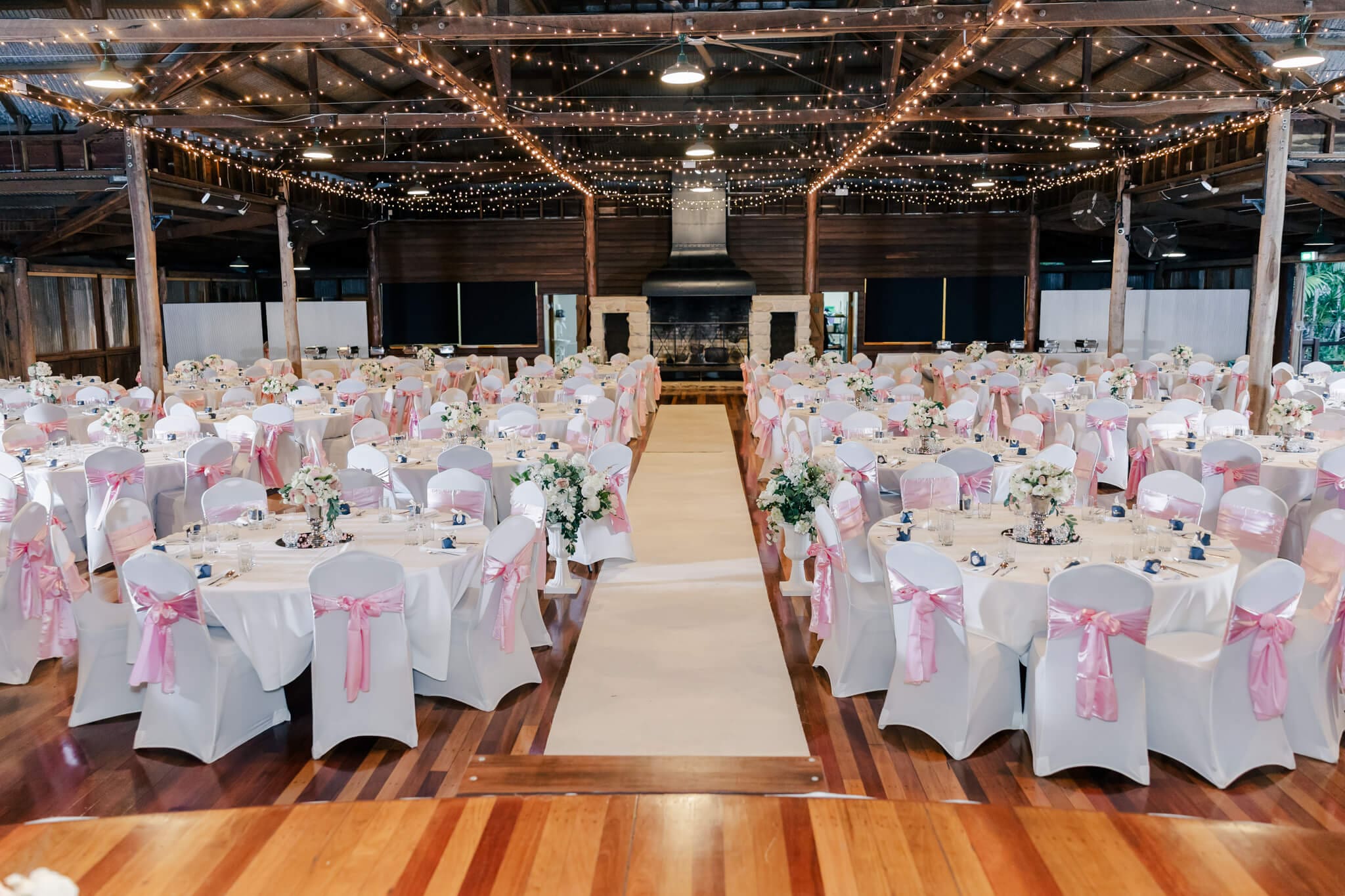 A wedding reception decorated by Stylish Events & Hire. White linen chair covers, pink bows and beautiful flowers in vases on the tables.