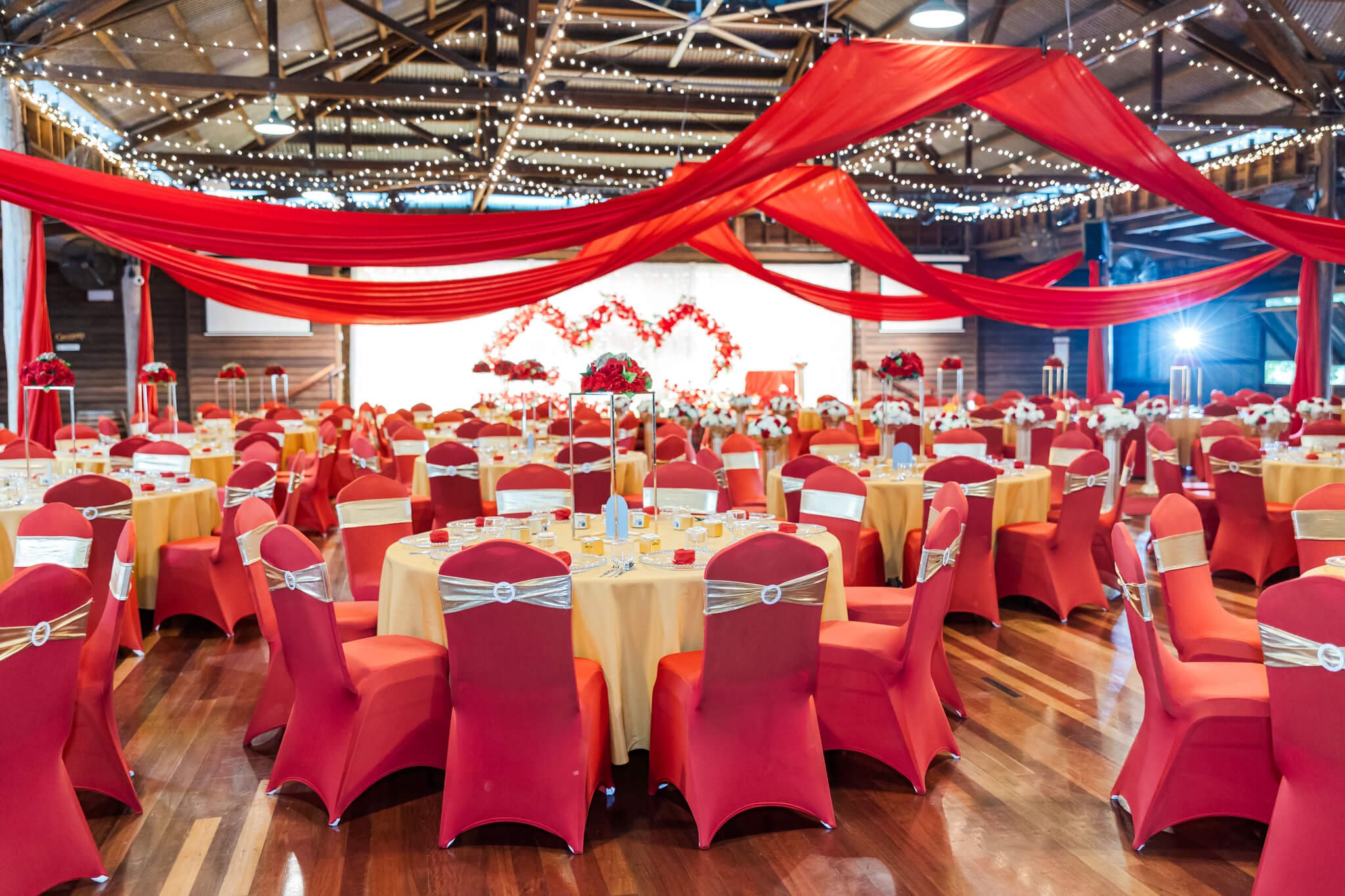 A wedding reception using wedding hire Rockhampton items. Reception tables, chairs, heavily decorated with red covers, gold tablecloths and red florals.