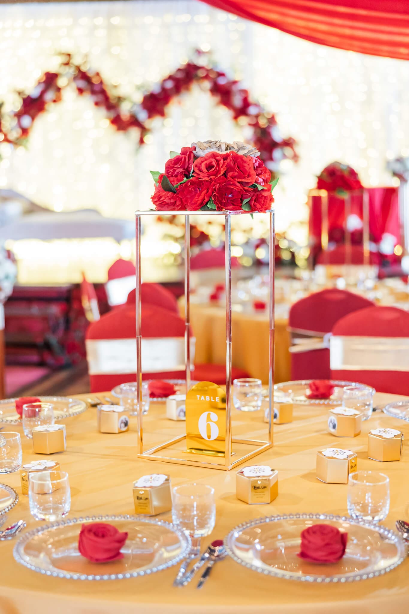 A centre piece for a wedding reception table featuring a gold centre piece with red flowers on top.