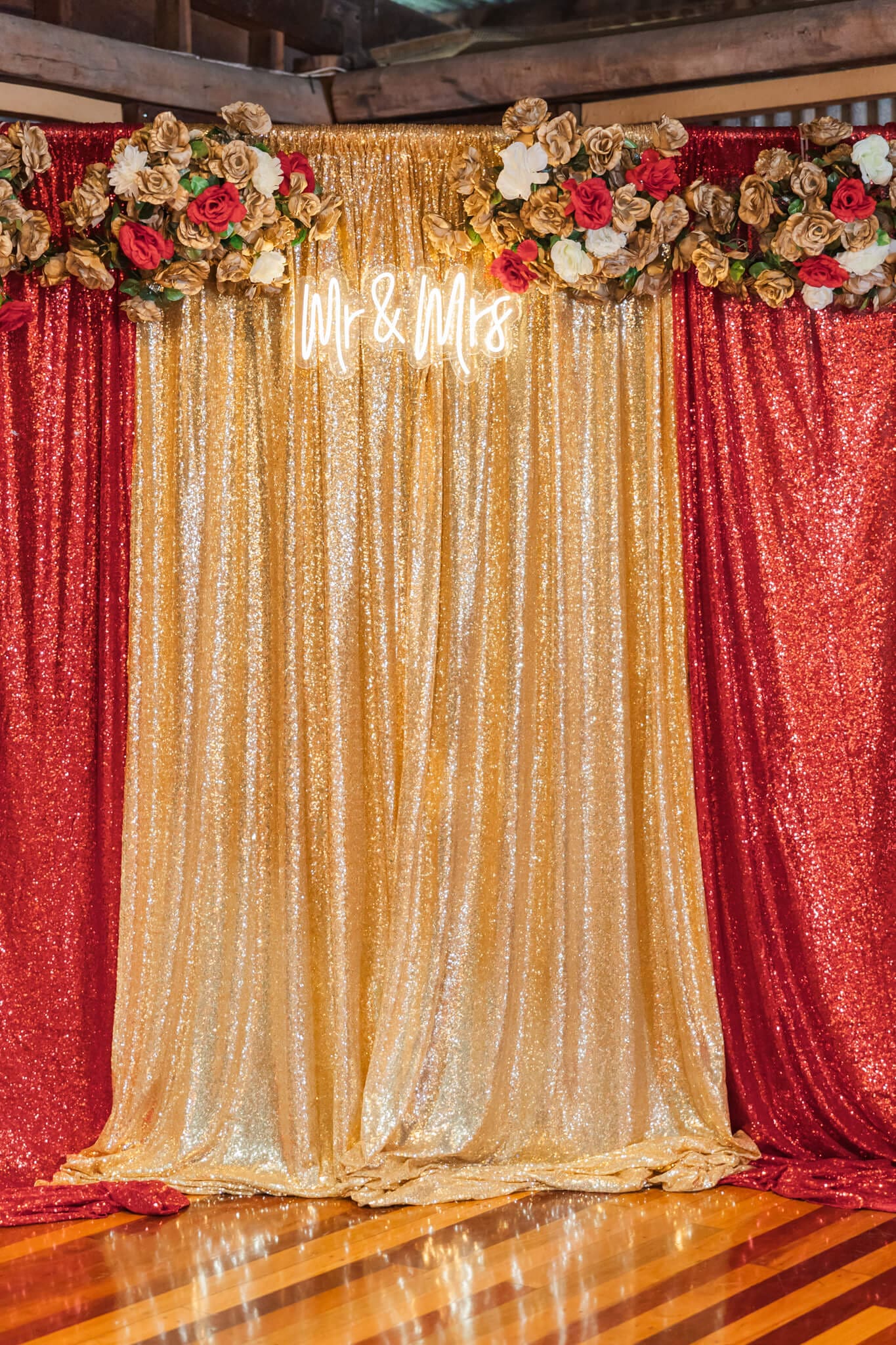 Gold and red sparkly photo booth curtain decorated with red, gold and white flowers along the top.