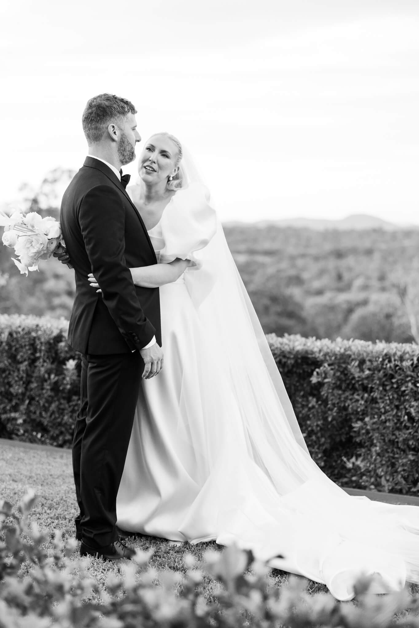 Black and white image in the style of editorial wedding photography of the bride and groom looking at one another.