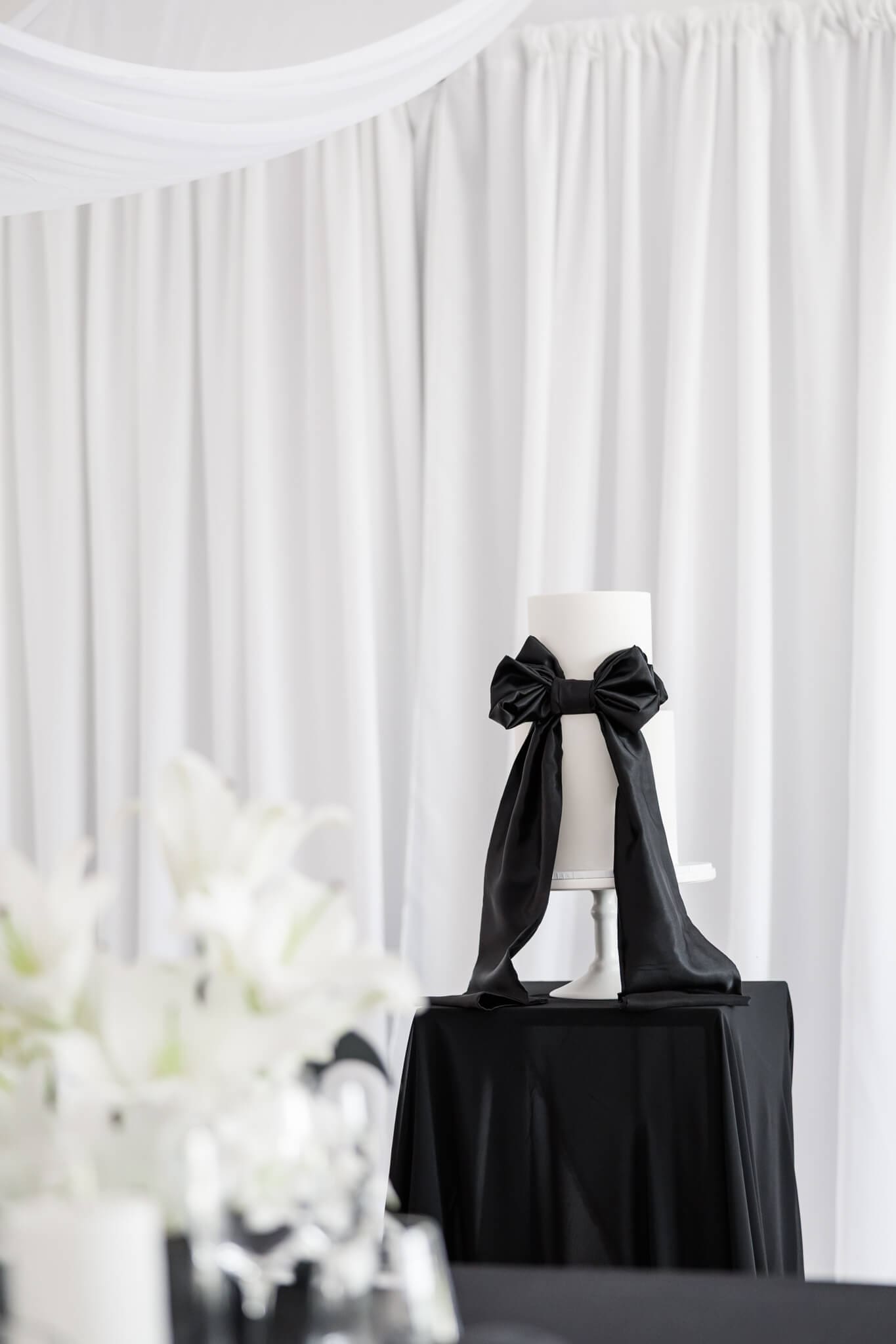 A black and white cake with a very large black bow made of icing.