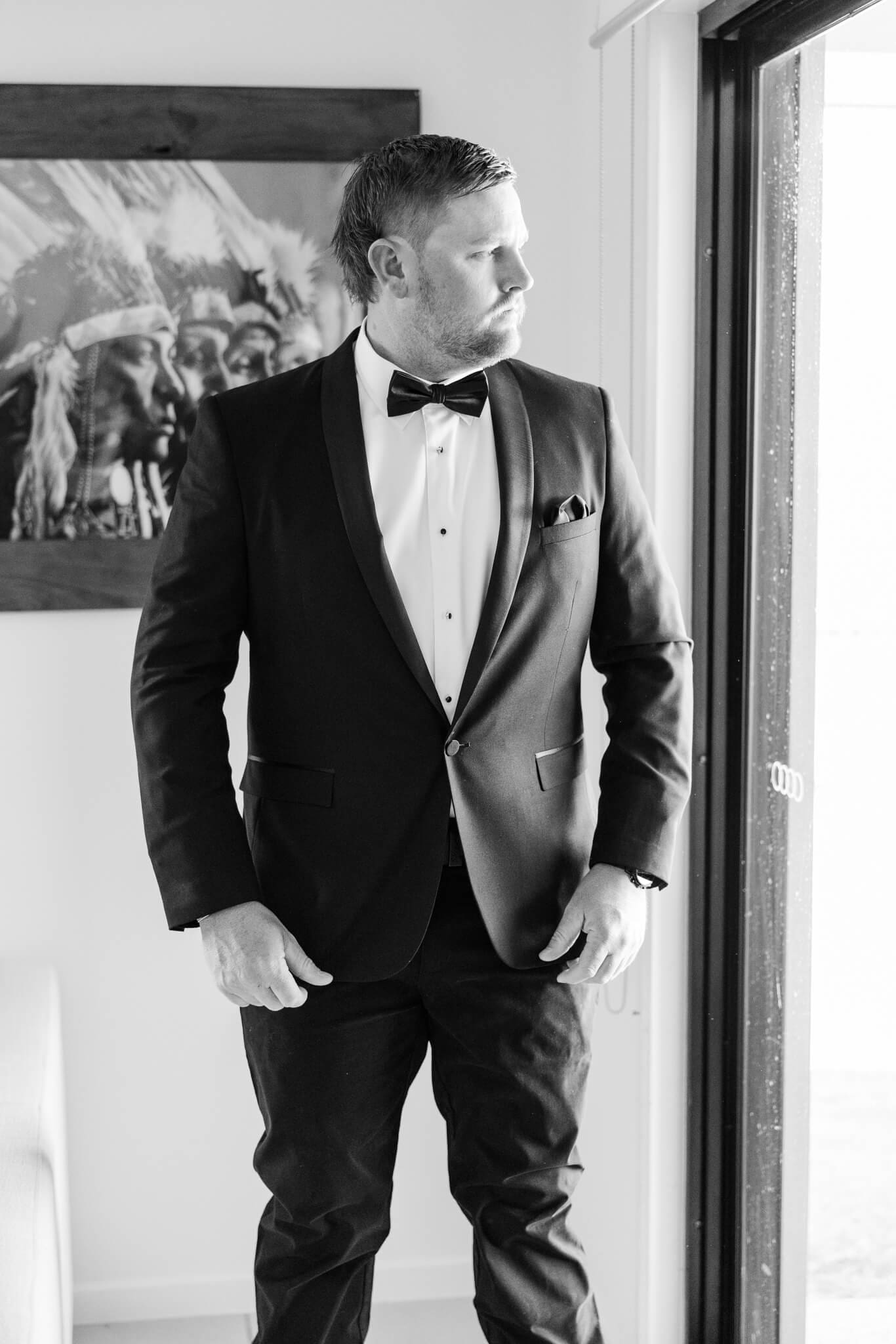 Editorial wedding photography style at it's best - a black and white image of the groom looking out the window beside him.