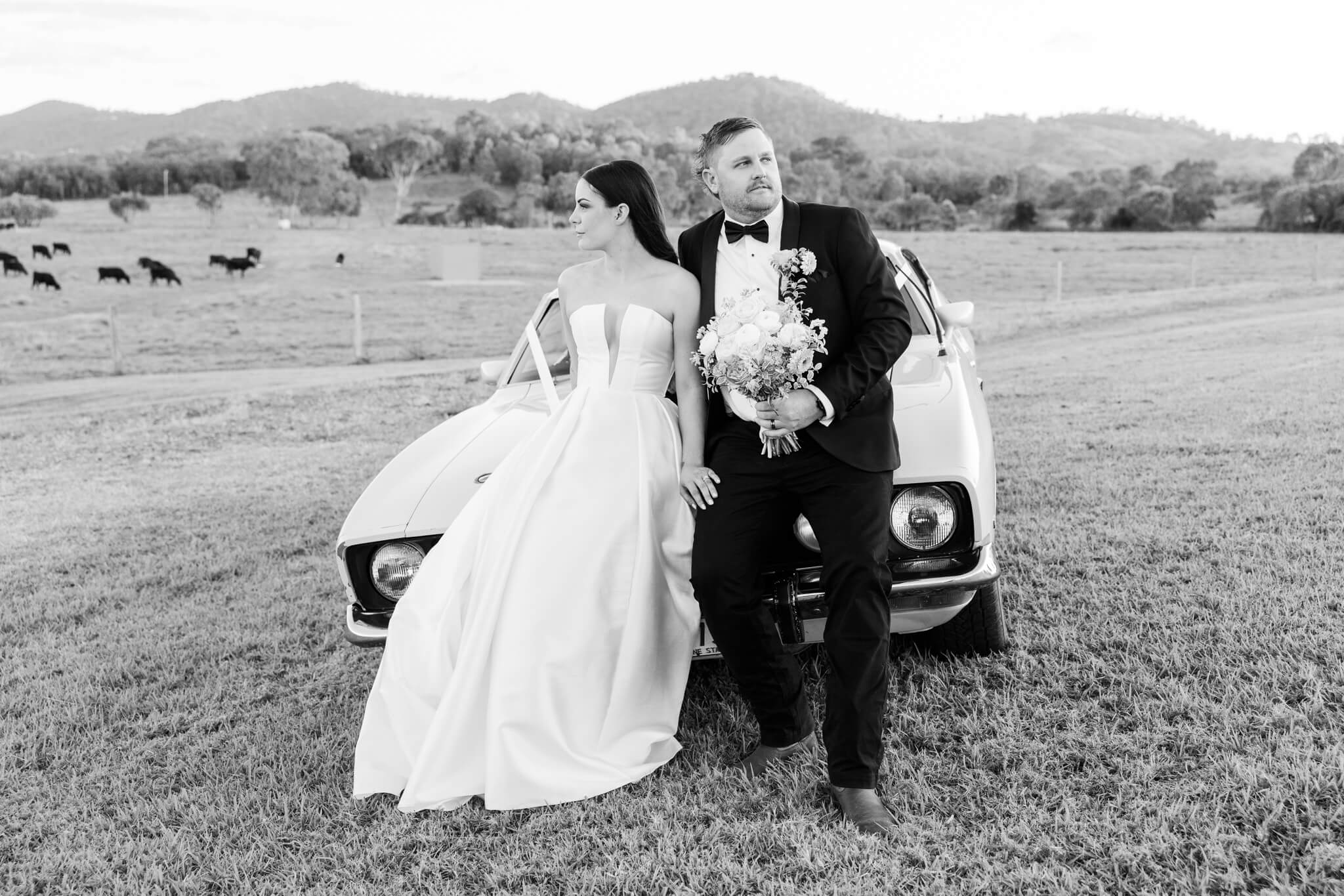 Bride and Groom pose on an old fashioned car's bonnet in true style of editorial wedding photography
